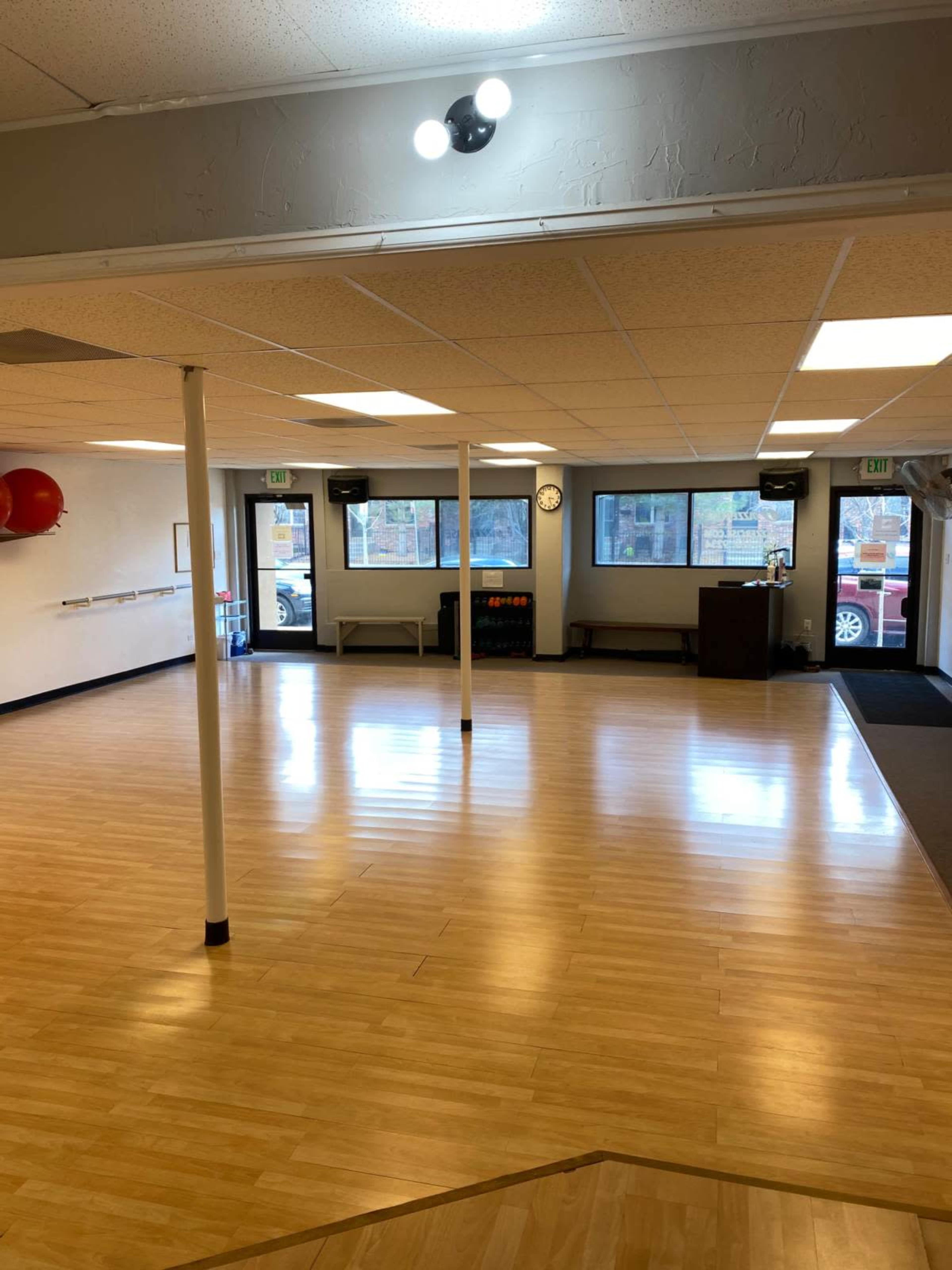 A spacious, empty room with wooden flooring, large windows, and minimal furnishings.