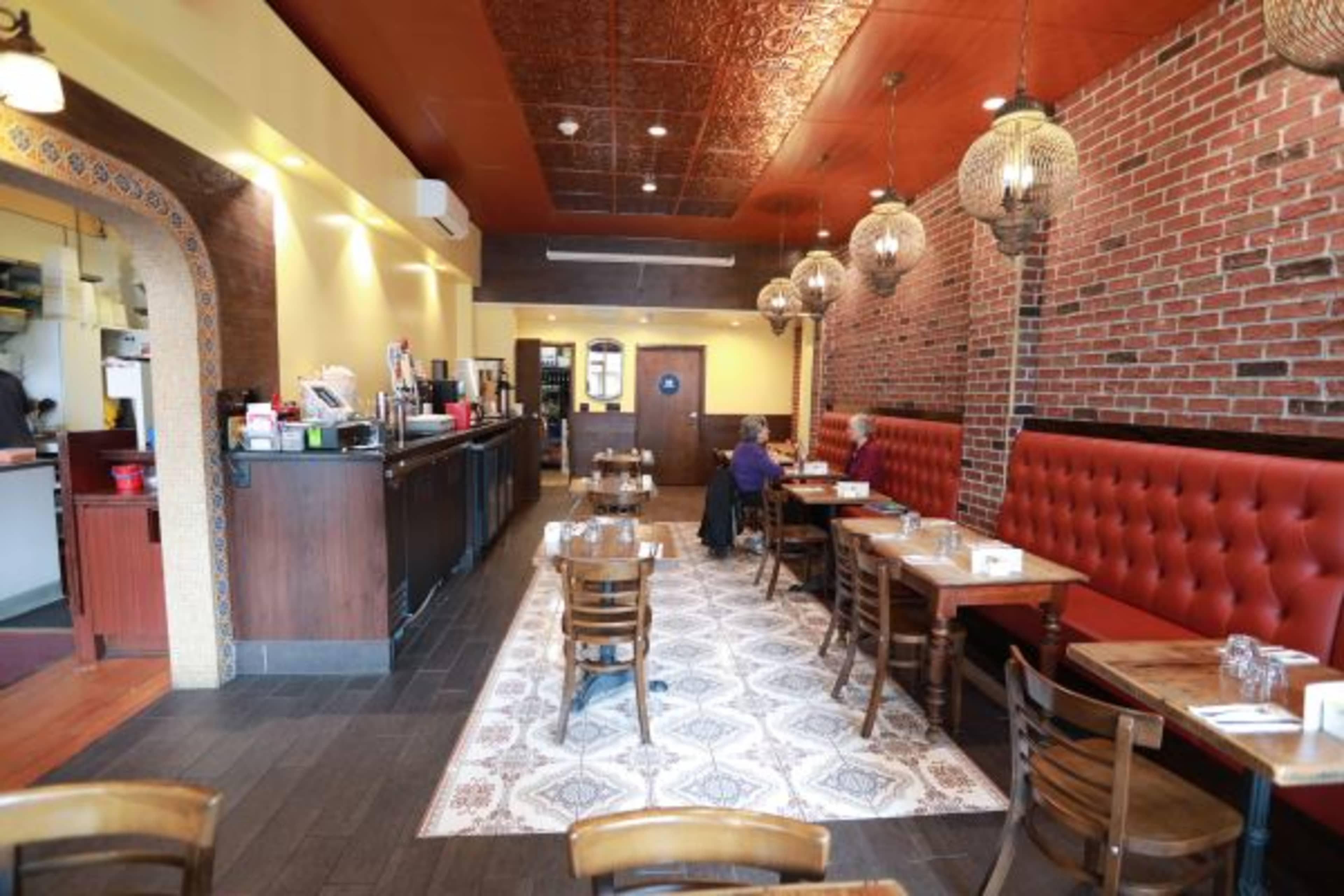 A cozy restaurant interior featuring a mix of red upholstered seating, wooden tables, and decorative lighting fixtures.