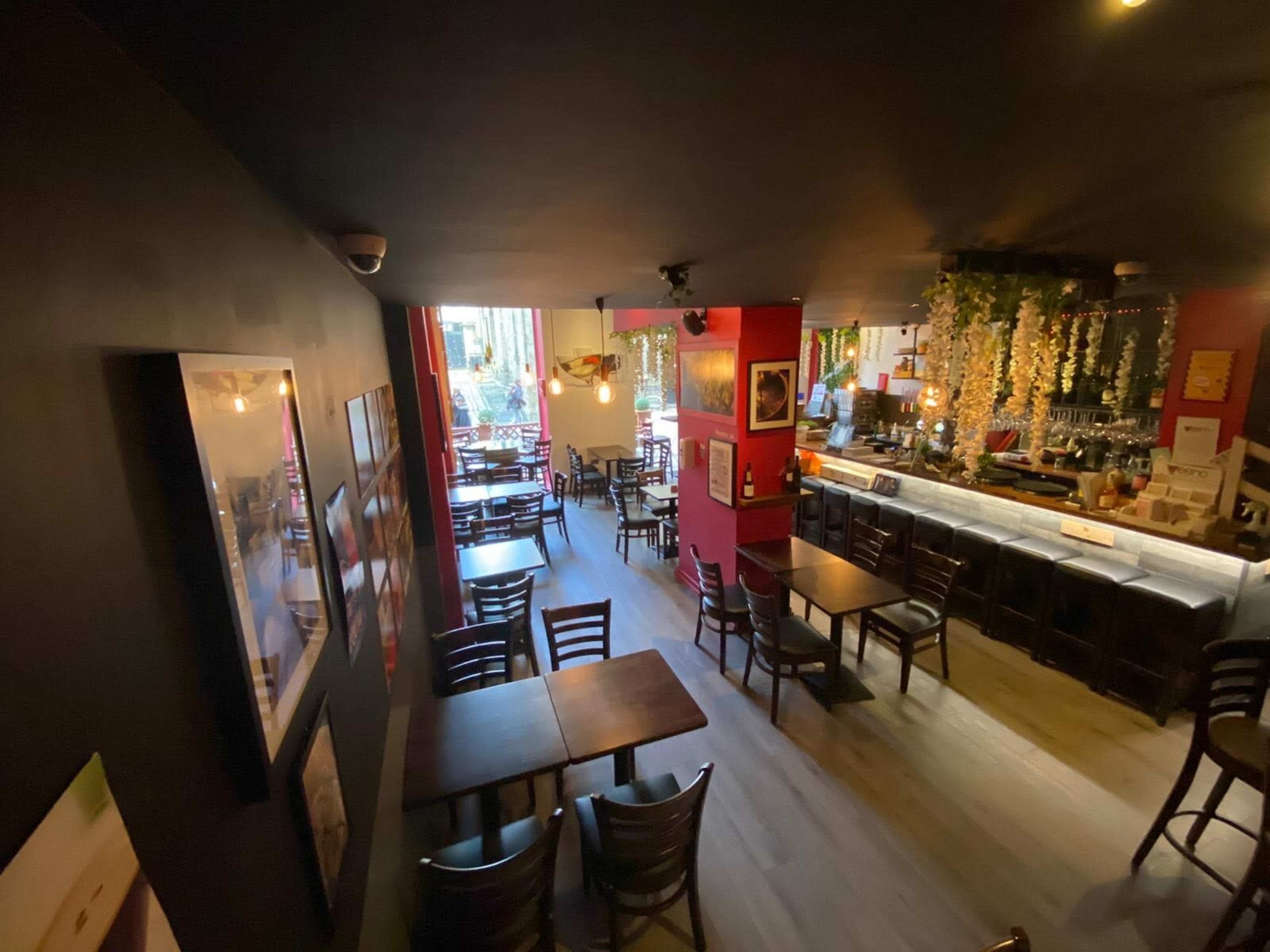 A cozy restaurant interior with wooden tables and chairs, a bar counter in the background, and large windows letting in natural light.