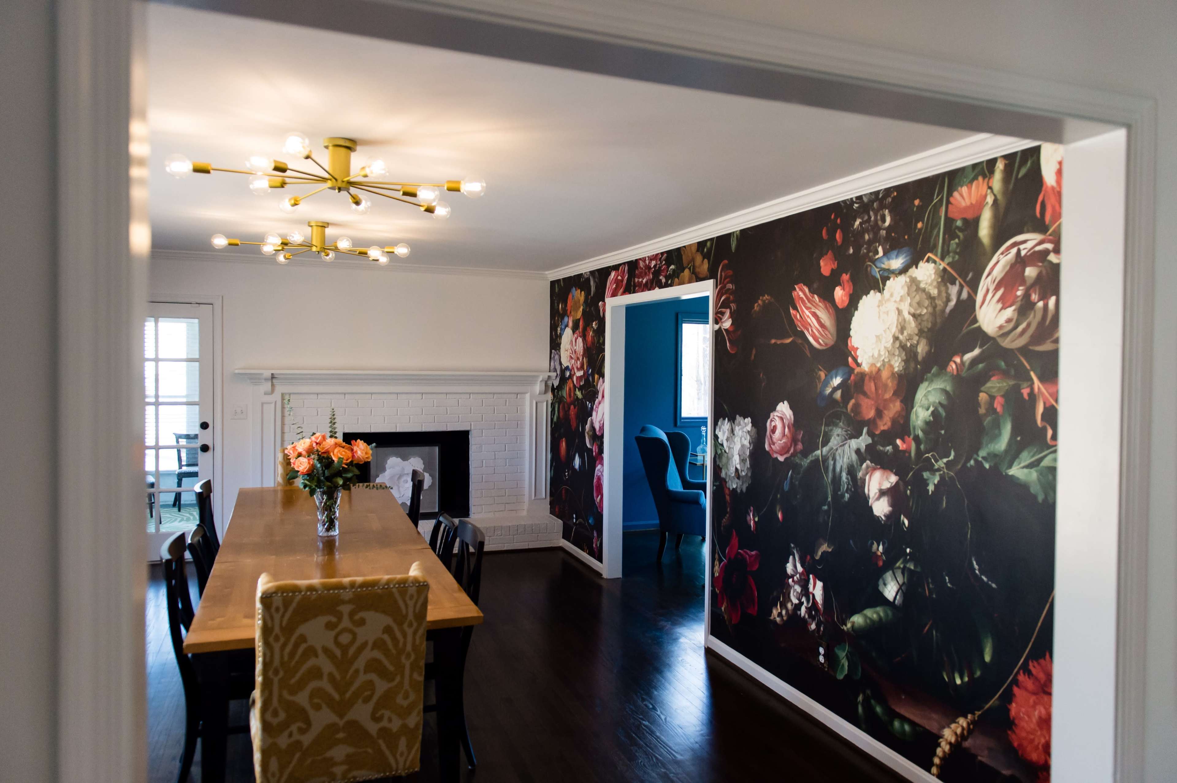 A dining room features a long wooden table with chairs and a wall adorned with a large floral mural.