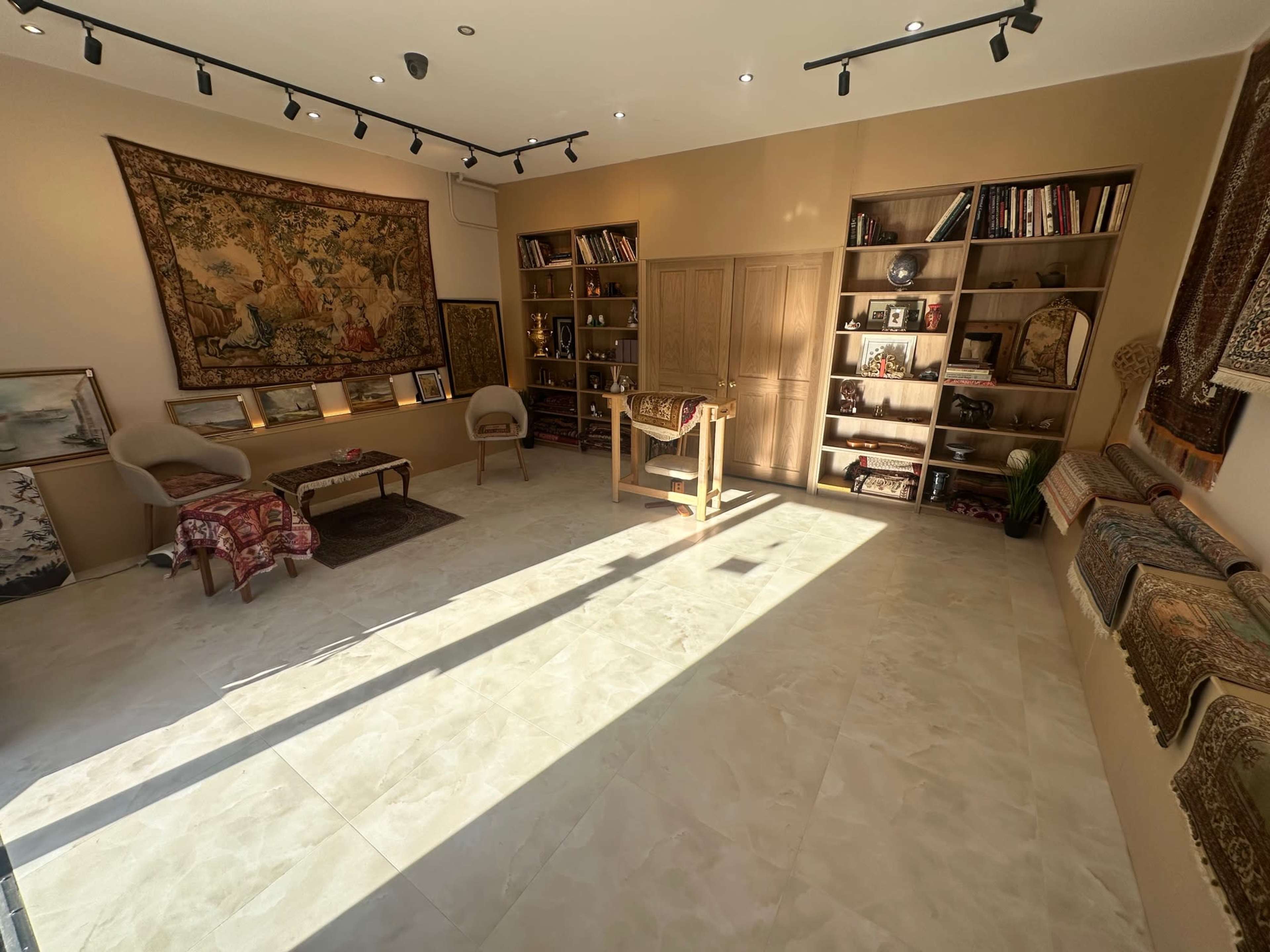 The image shows a well-lit interior of an art gallery or showroom featuring shelves filled with decorative items and artworks, along with a central table and seating arrangements.