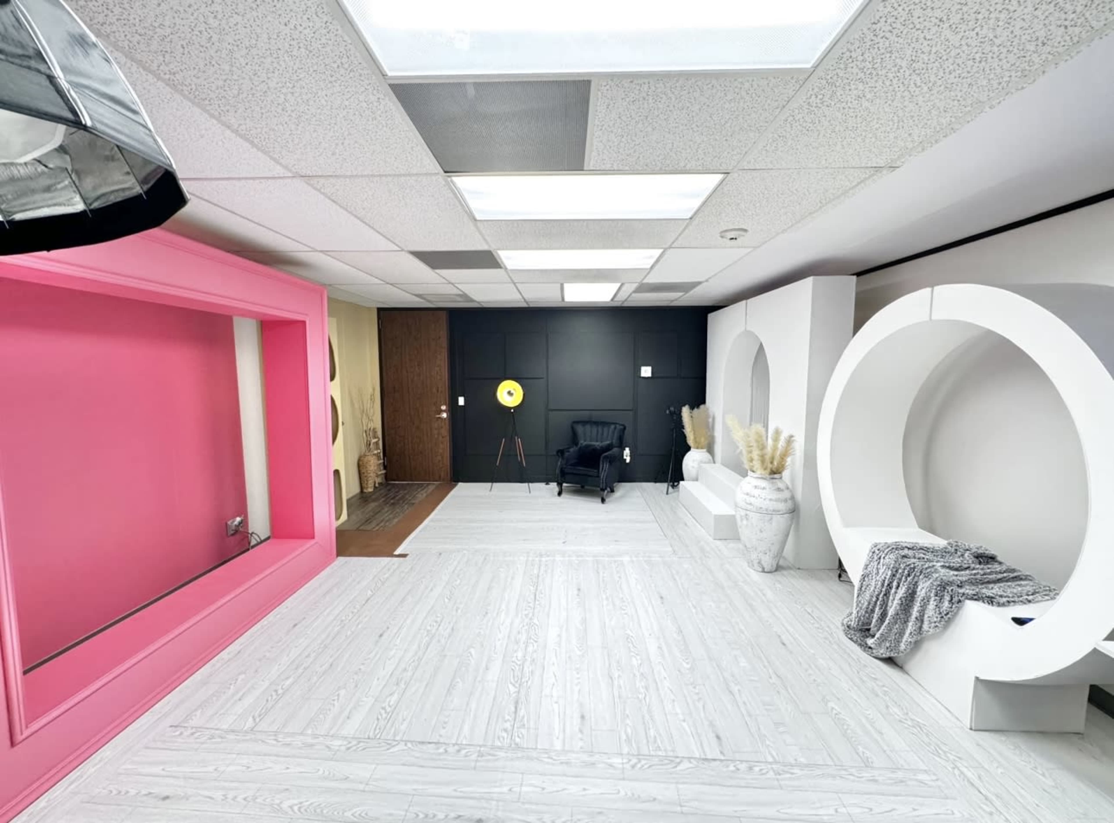A modern studio space with a black accent wall, a large pink frame, a white circular structure, and a chair with decorative elements arranged neatly.