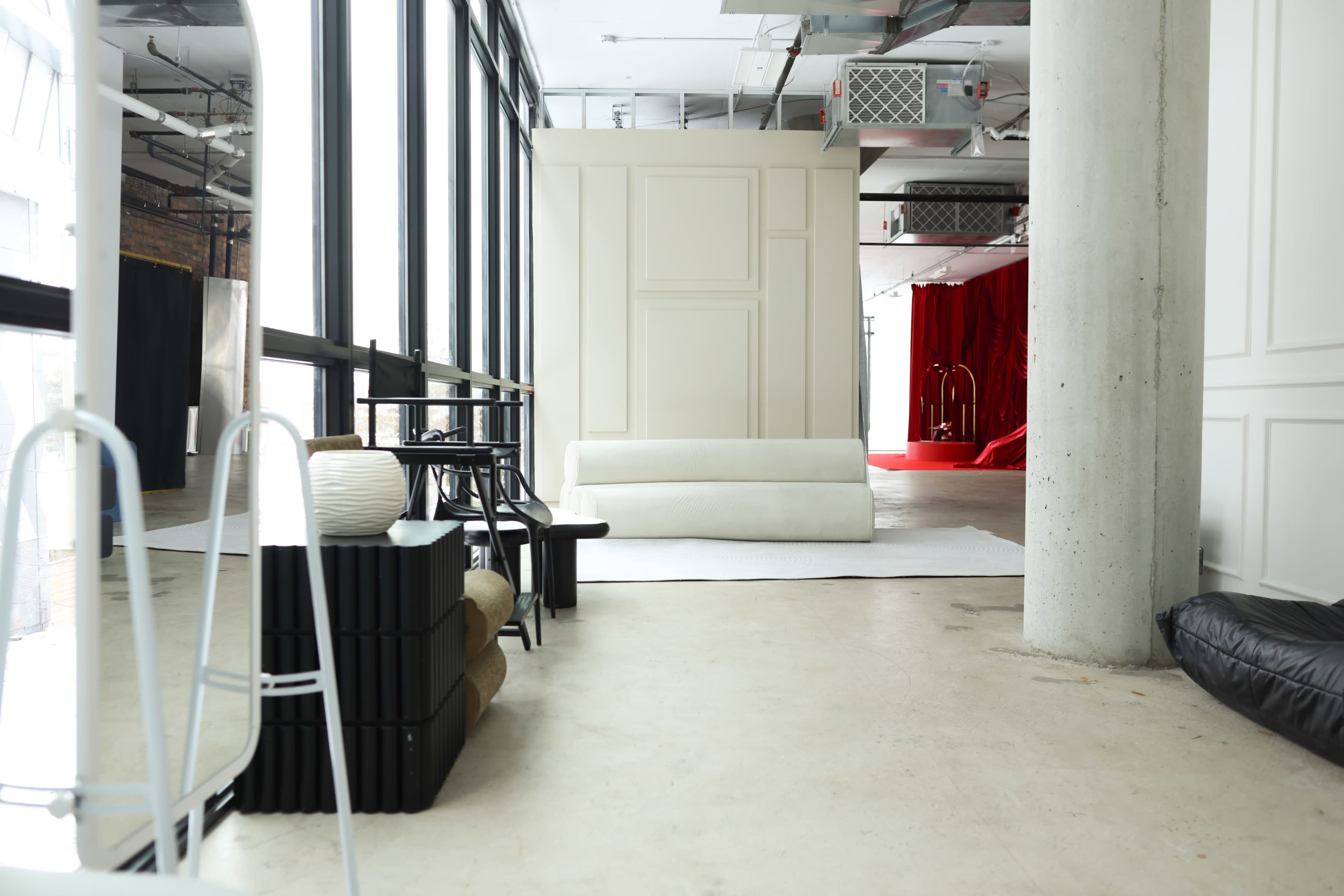 The scene shows a spacious interior with large windows, featuring a white lounge area and a red backdrop towards the back.