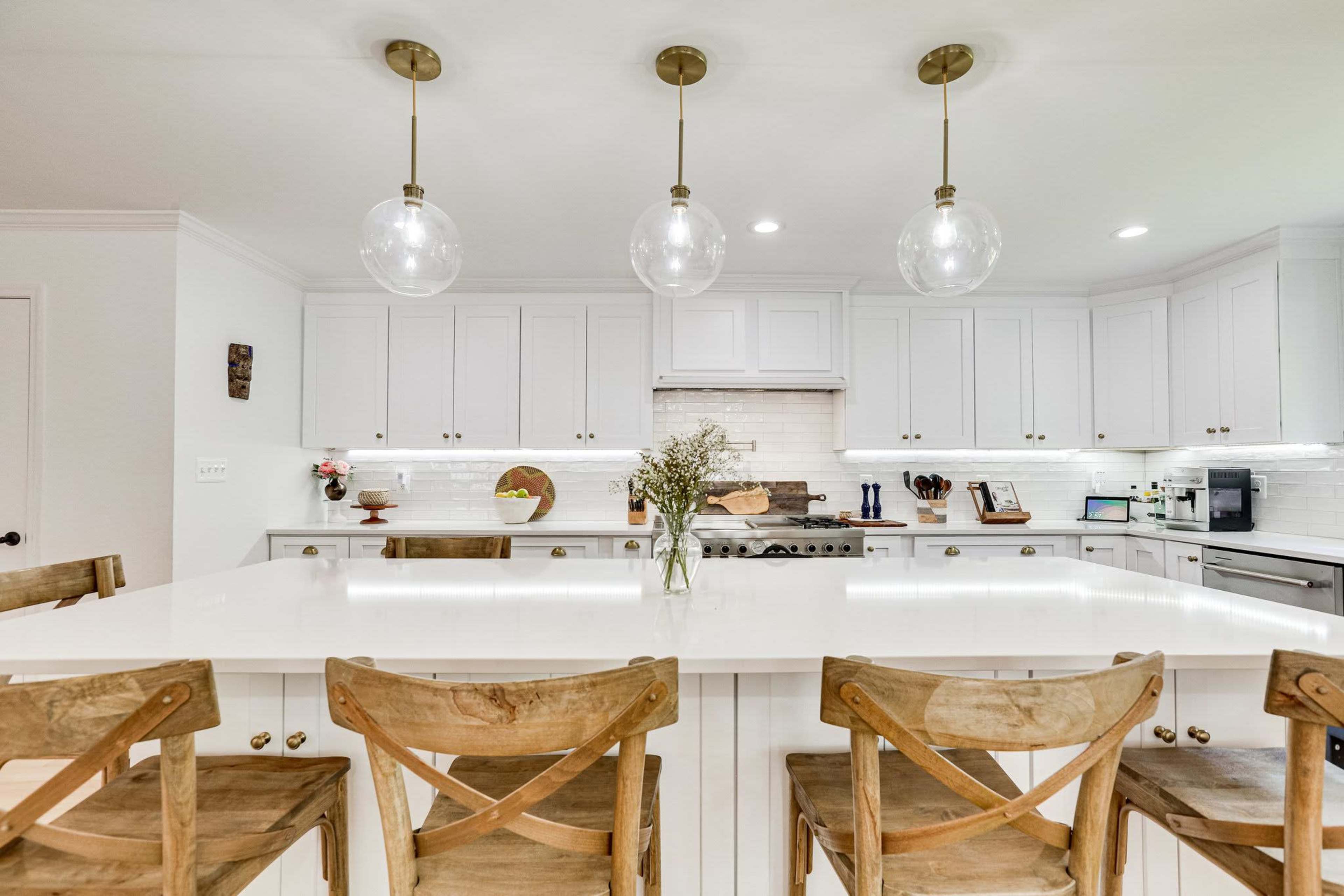 A modern kitchen features white cabinets, a large island with wooden stools, and pendant lighting above.