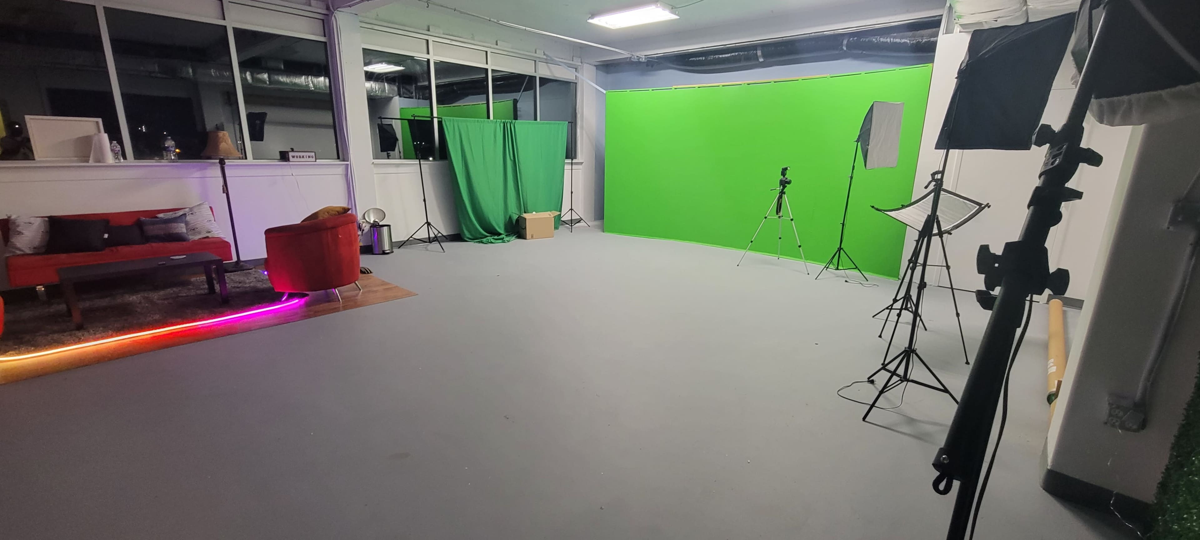 A spacious studio with a green screen setup, a red couch, and various photography equipment arranged around the room.