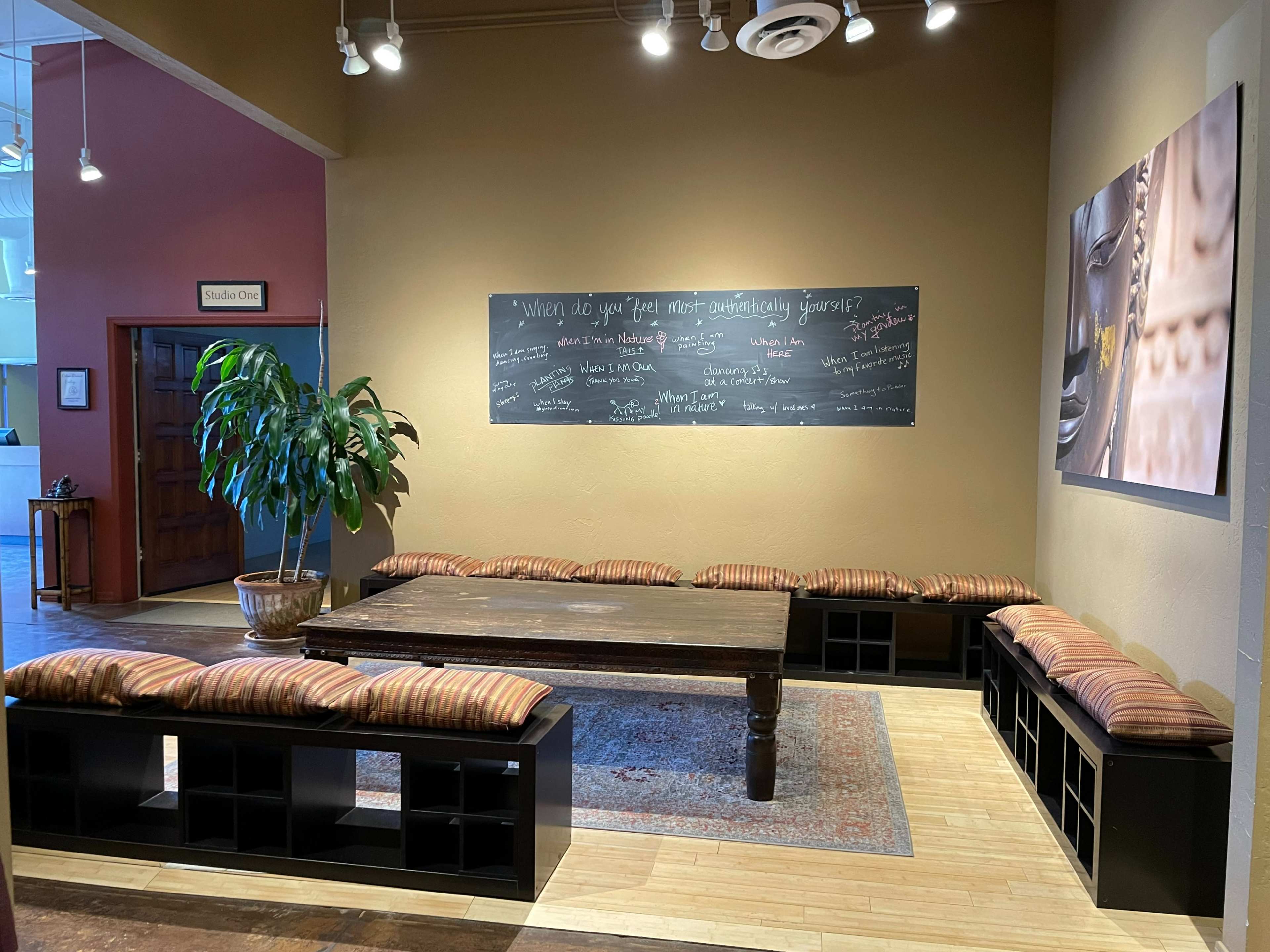A cozy lounge area with a large wooden table surrounded by cushioned benches and a chalkboard on the wall with various writings.