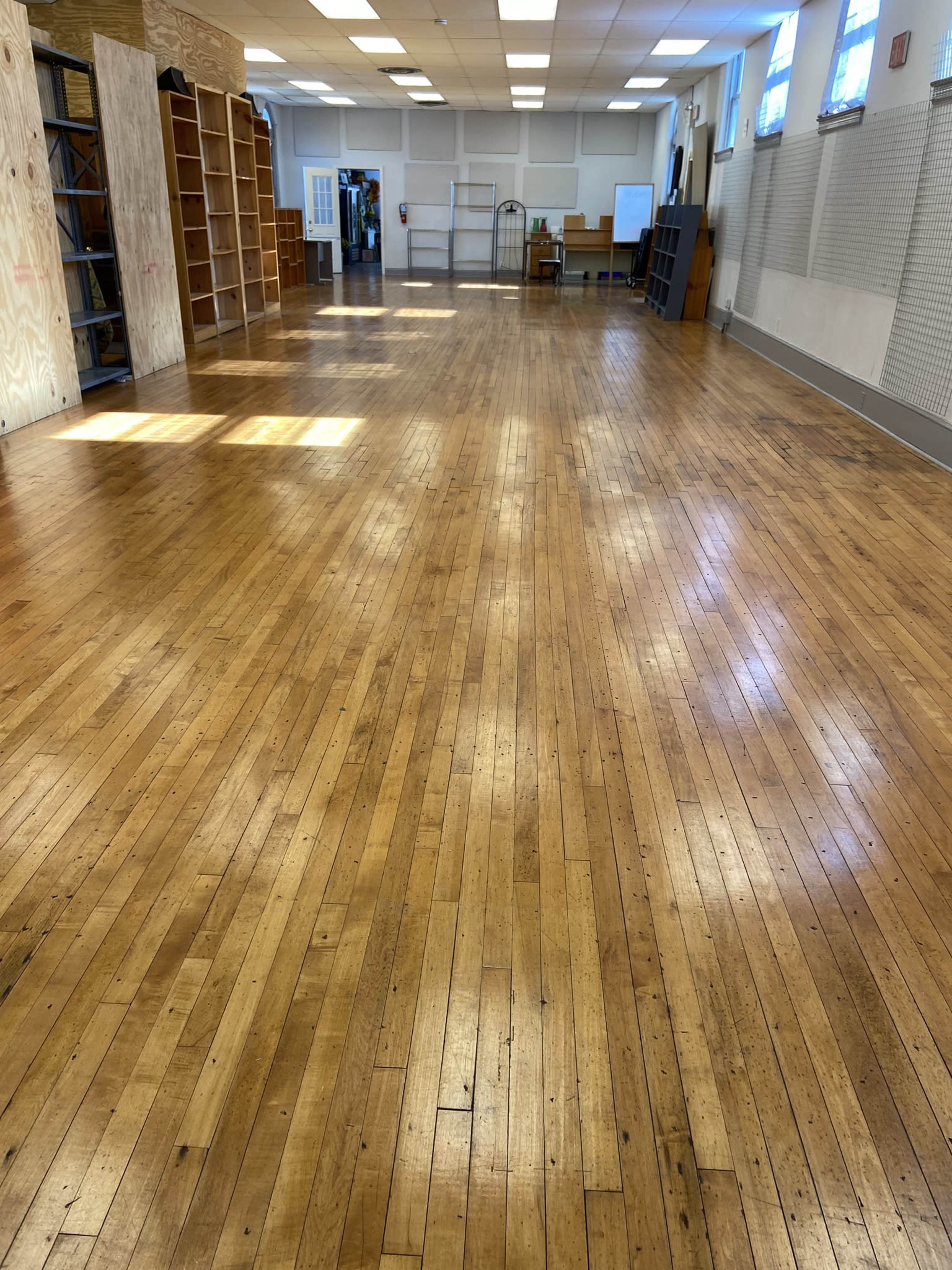 The image shows a spacious room with polished wooden floors and shelves along the walls.