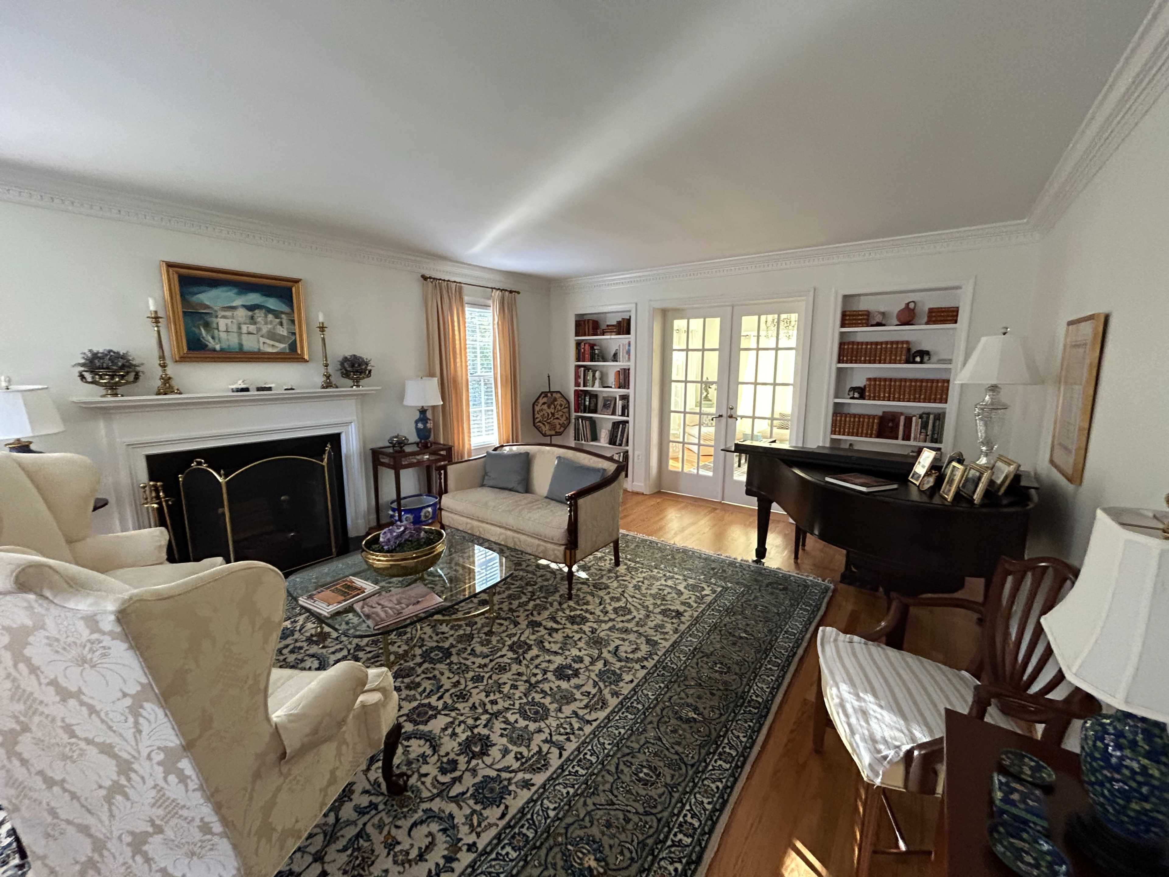 A tidy living room with a fireplace, a piano, bookshelves, and a large area rug.