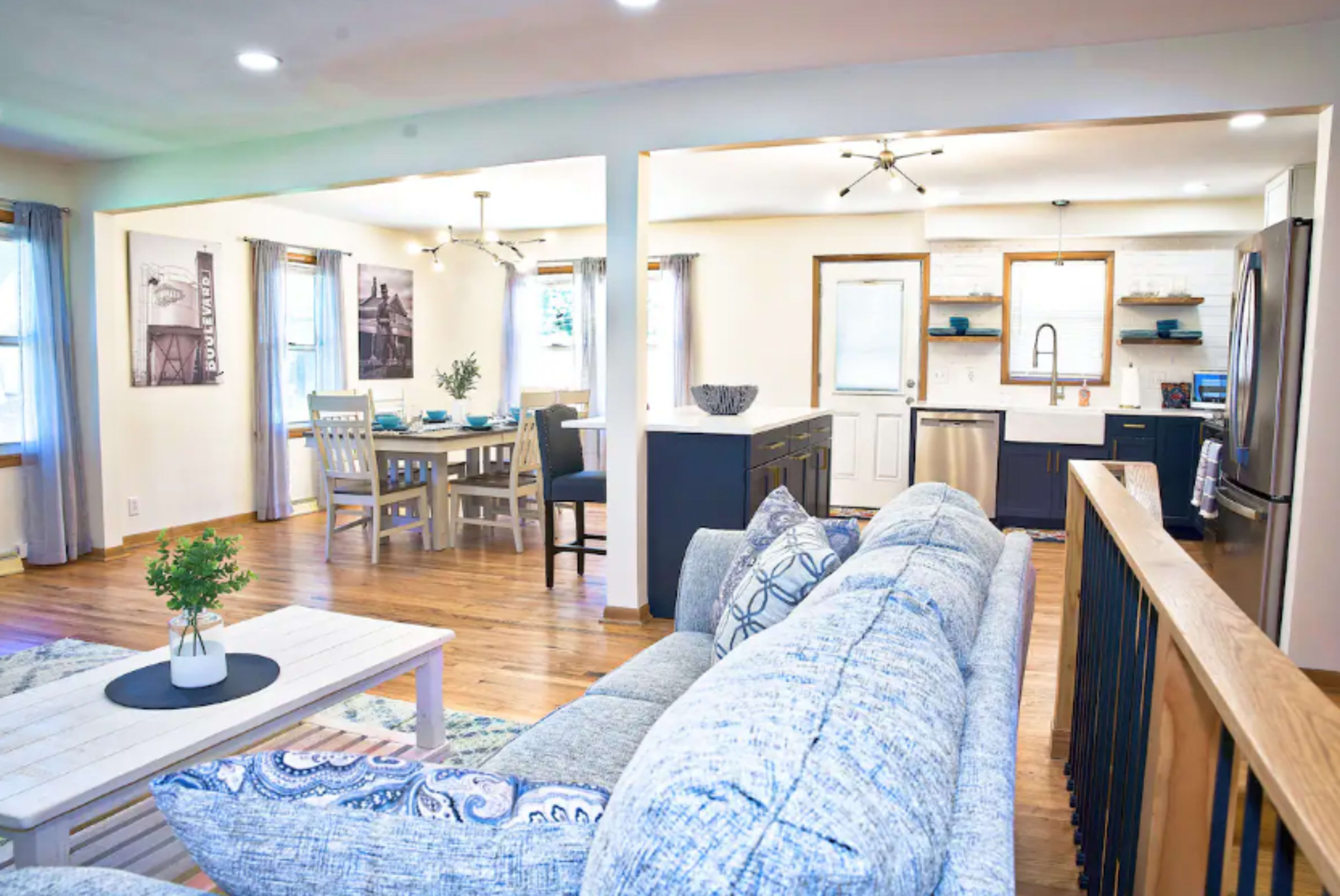A modern living room features a comfortable couch and a view into a well-lit kitchen and dining area.