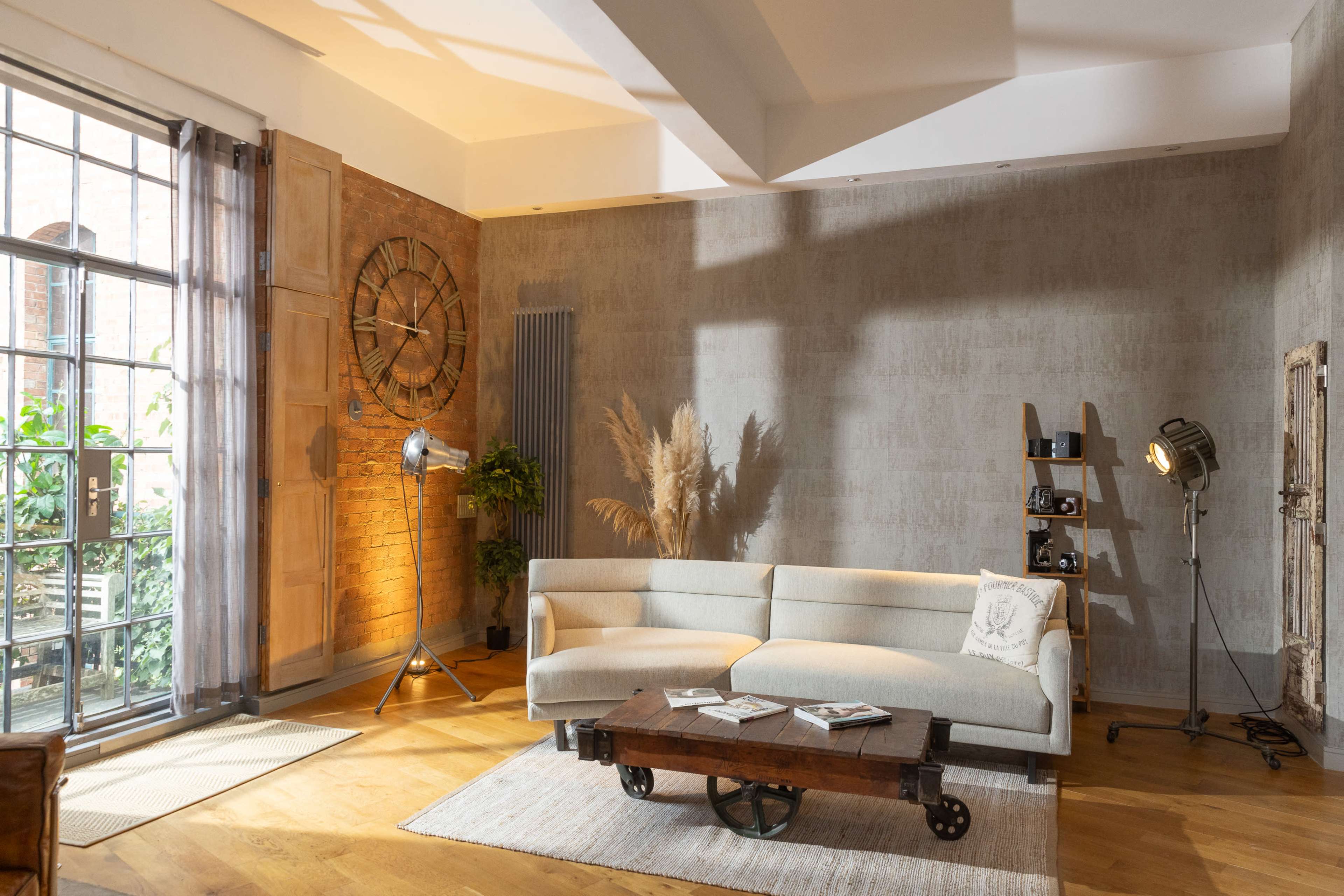 The image features a modern living room with a light gray sofa, a wooden coffee table, and large windows that allow natural light to flood the space.