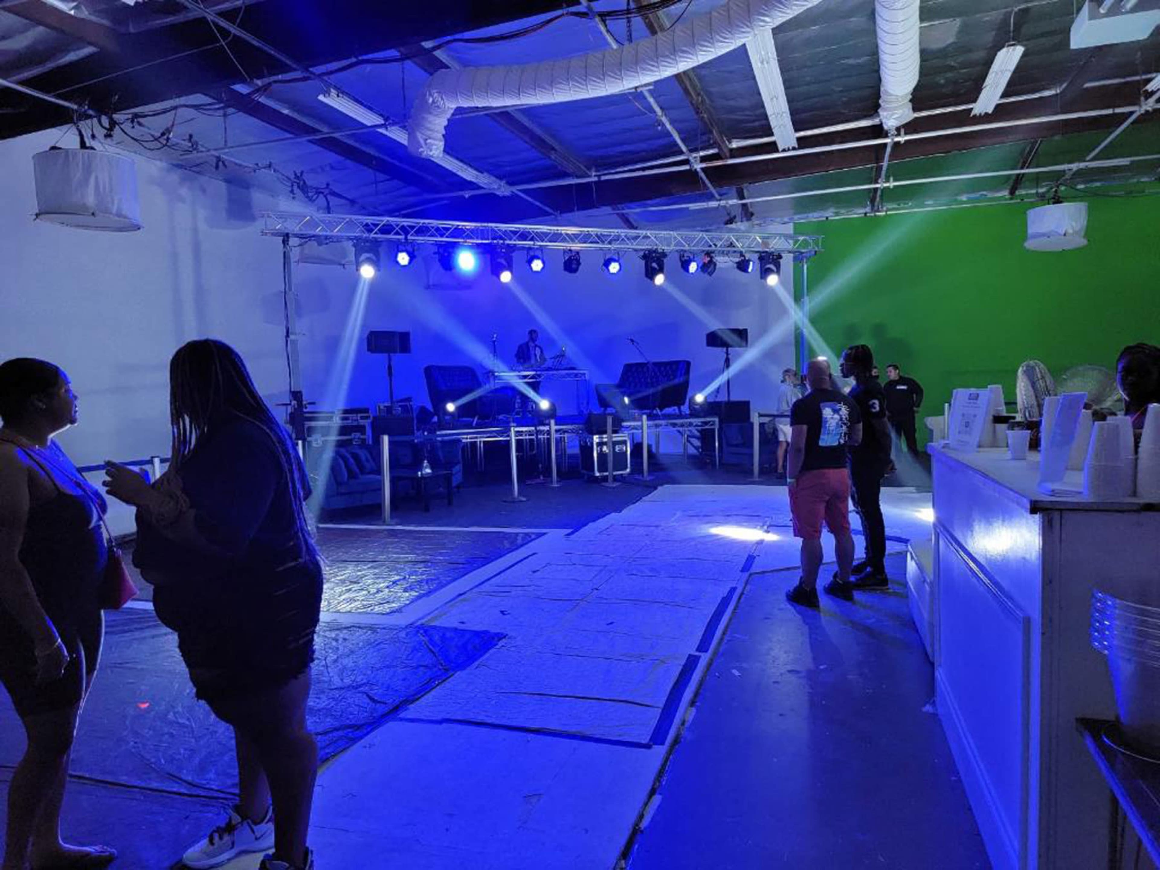 An indoor event space with a DJ setup featuring lights, a dance floor area, and people socializing.