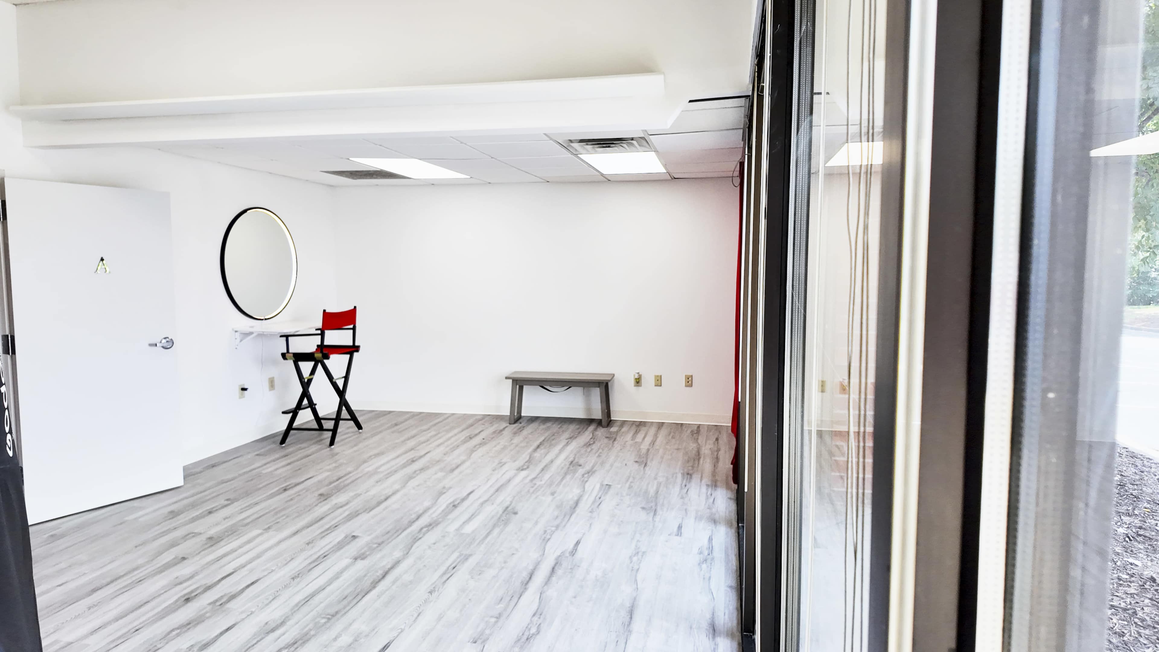 A sparse room with light wood flooring, a large mirror on the wall, a red director's chair, and a low table.