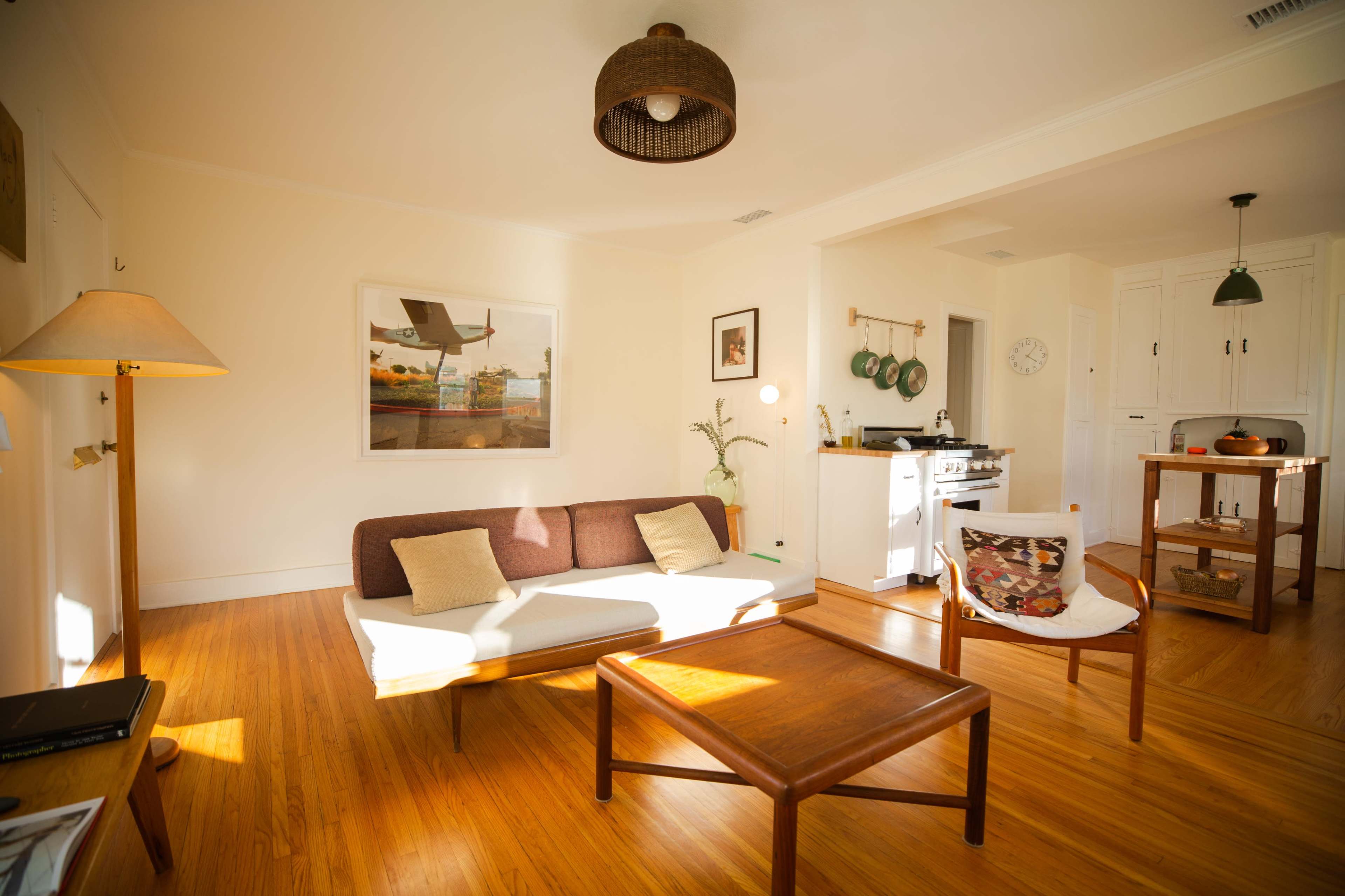 The image shows a well-lit living space featuring a brown sofa, a wooden coffee table, and a dining area with a small table and chairs.