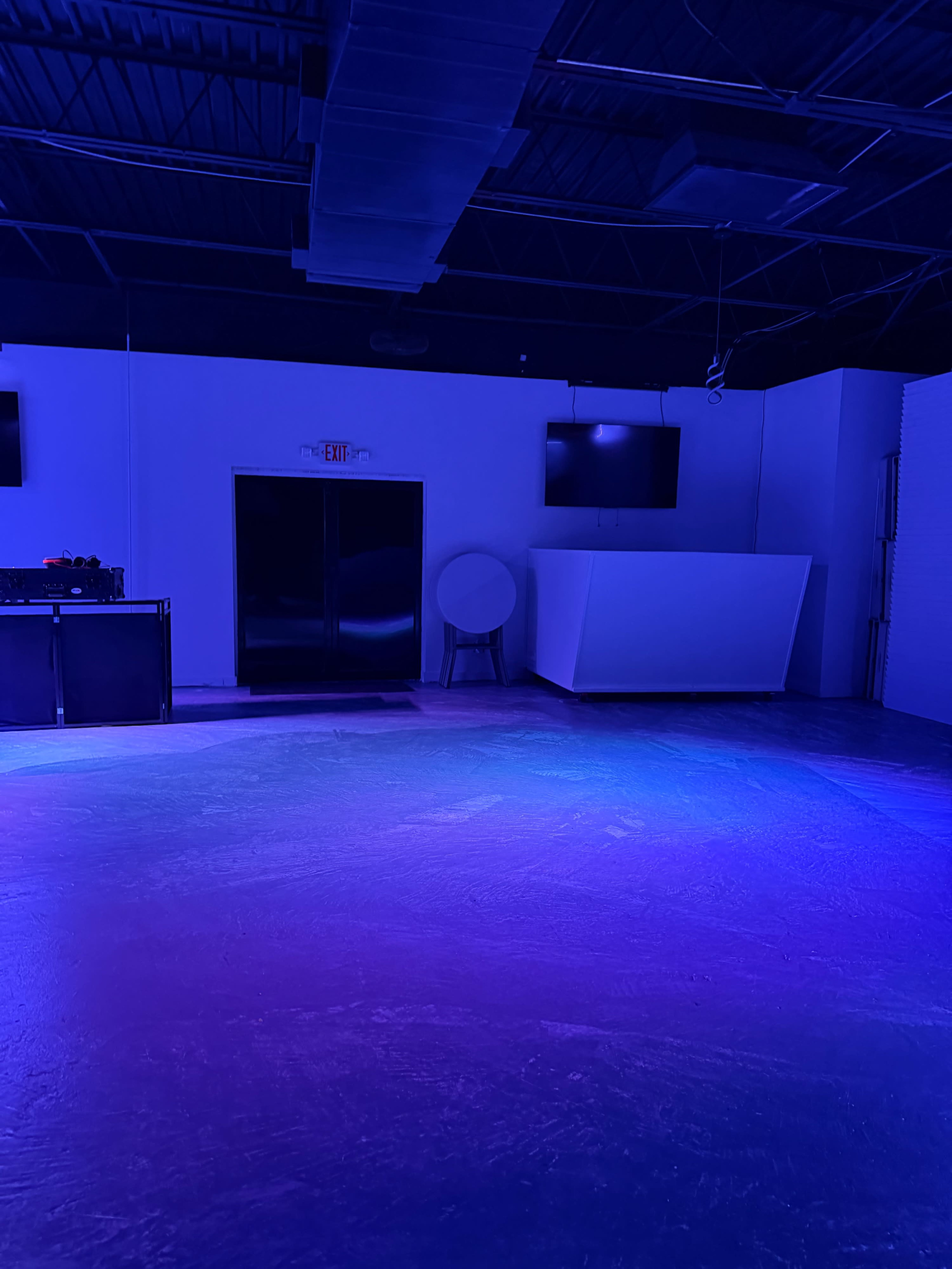 The image shows an empty room with blue and purple lighting, featuring a closed door, a circular table, and a solid white wall.