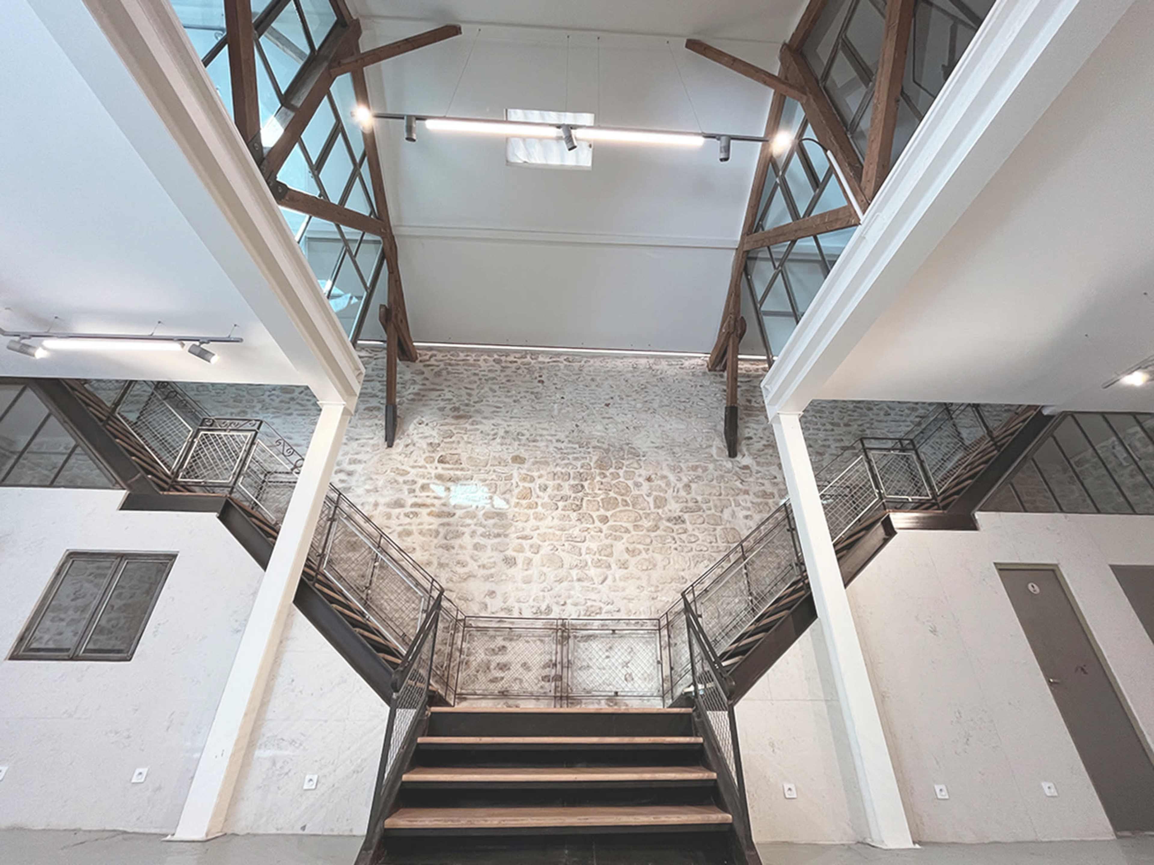 A spacious interior with a large, exposed brick wall flanked by two wooden staircases leading to a mezzanine level.