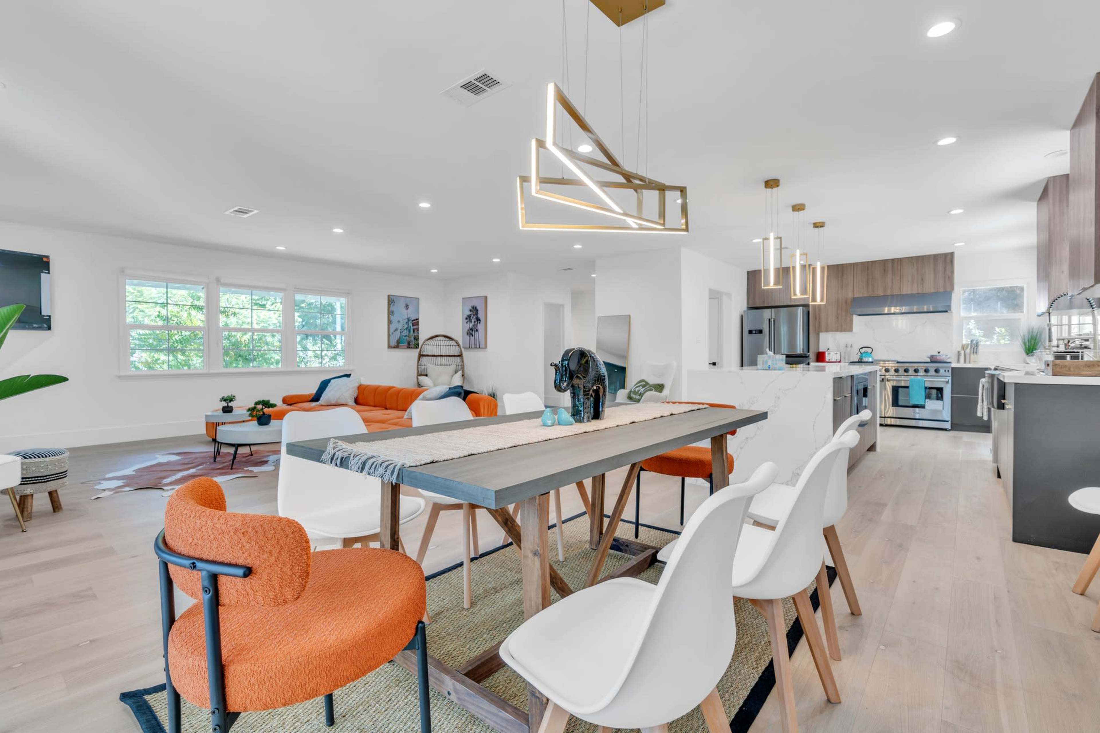 A modern open-concept living area features a dining table, contemporary chairs, and a large kitchen with stainless steel appliances.