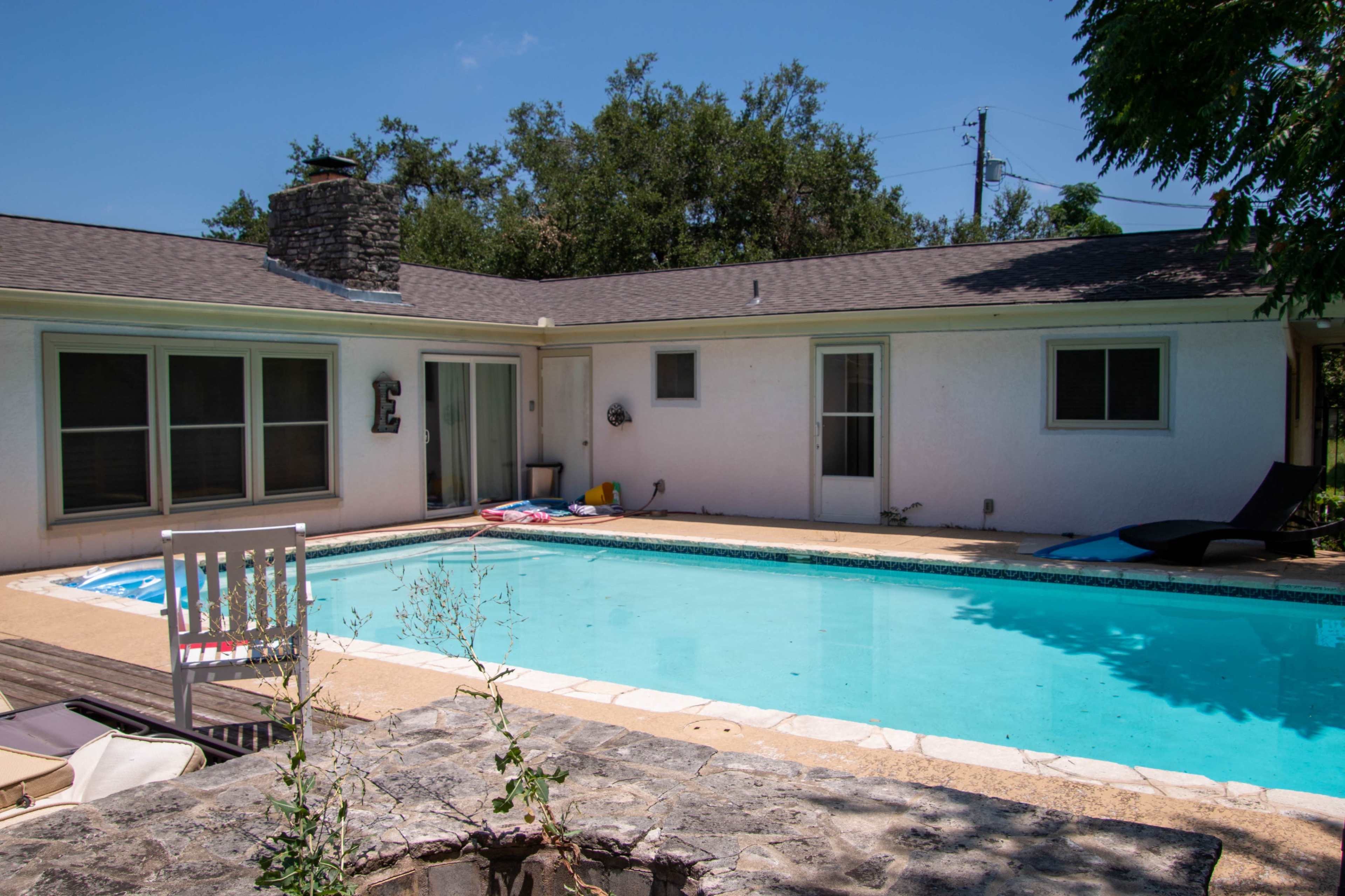The image shows a residential backyard featuring a swimming pool surrounded by concrete and a small patio area with lounge chairs.