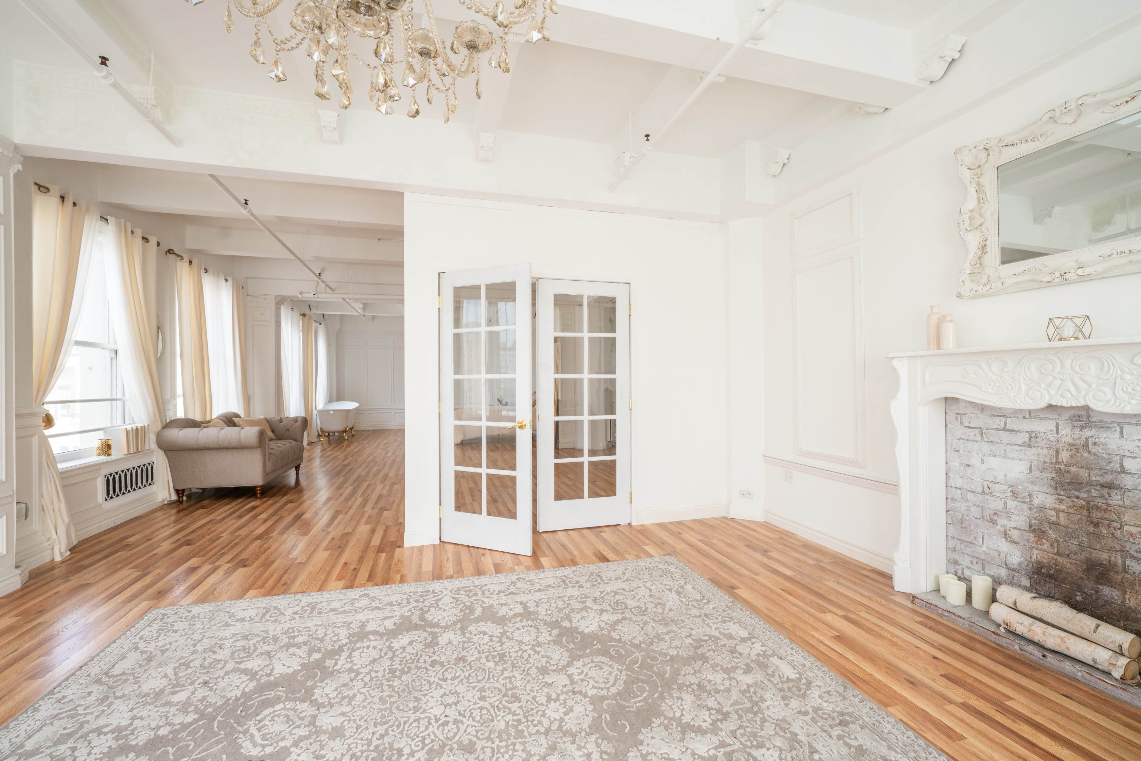 A bright, spacious interior with wooden floors, a decorative fireplace, and double French doors leading to another room.