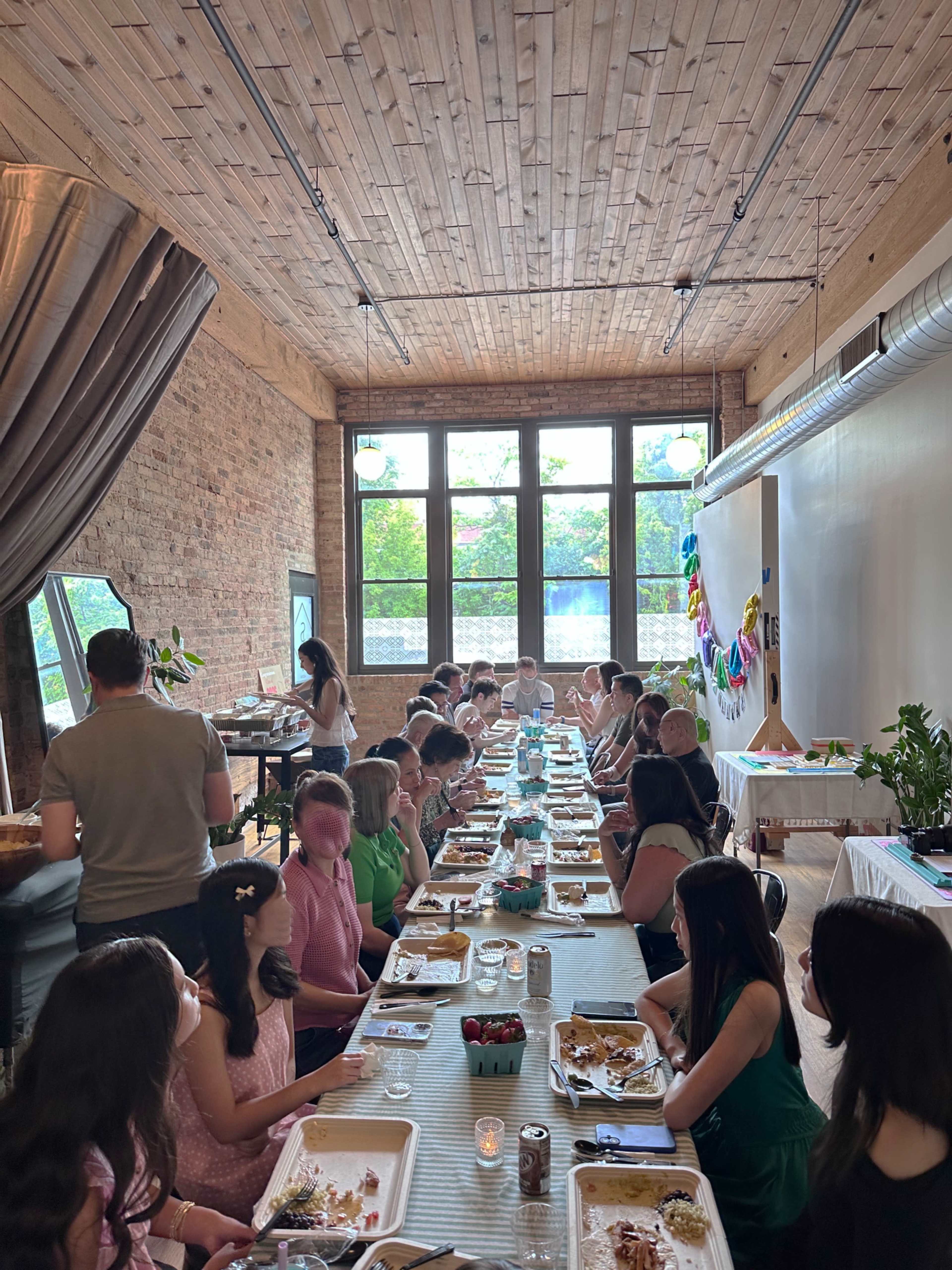 A long dining table is set in a bright, airy room filled with people enjoying a meal together.