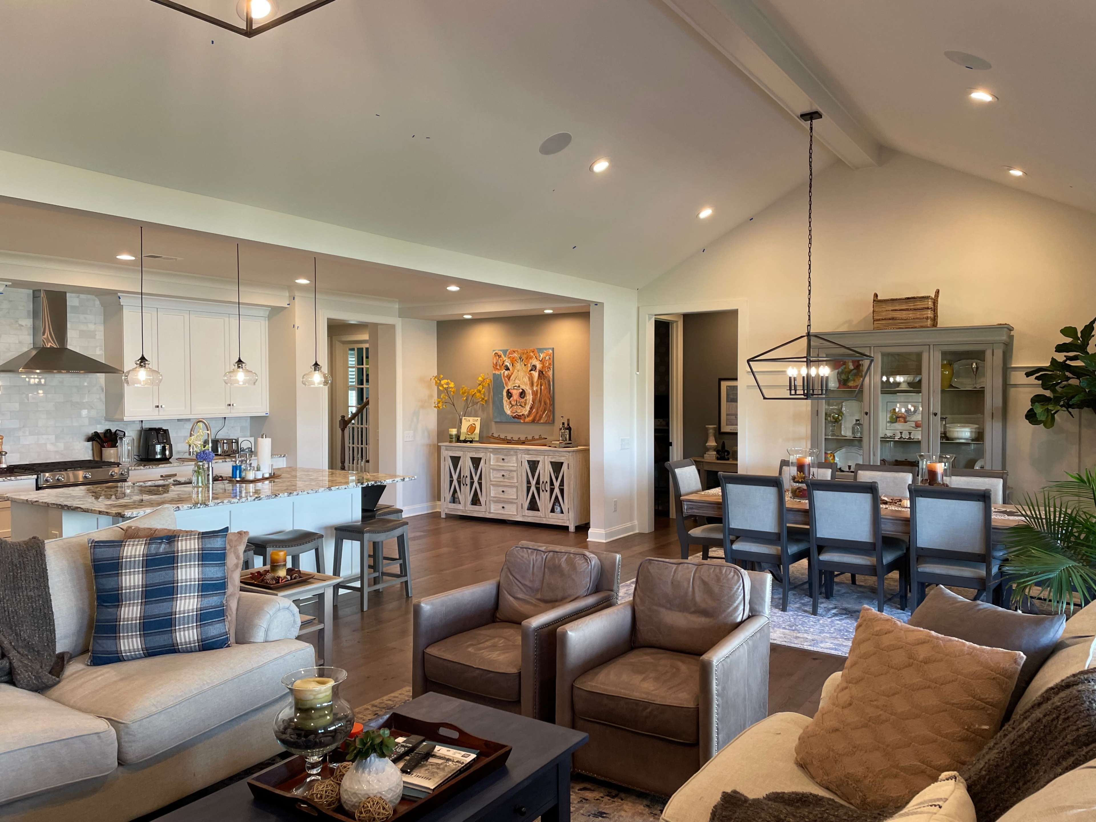 A spacious, modern living room and dining area featuring a comfortable sofa, armchairs, a dining table, and a kitchen with a large island.