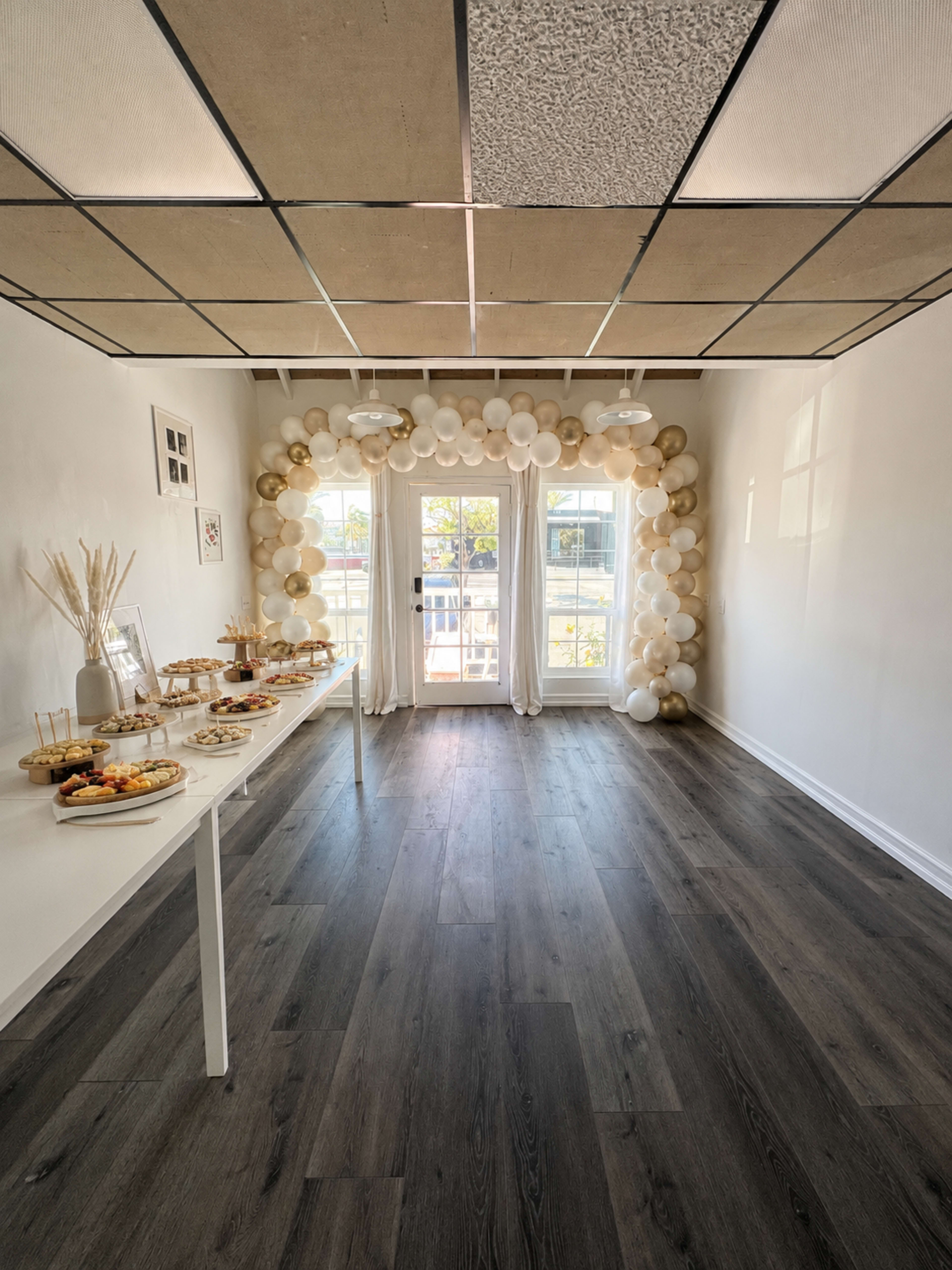 The image shows a decorated room featuring a table with food and a balloon arch over a set of doors leading outside.