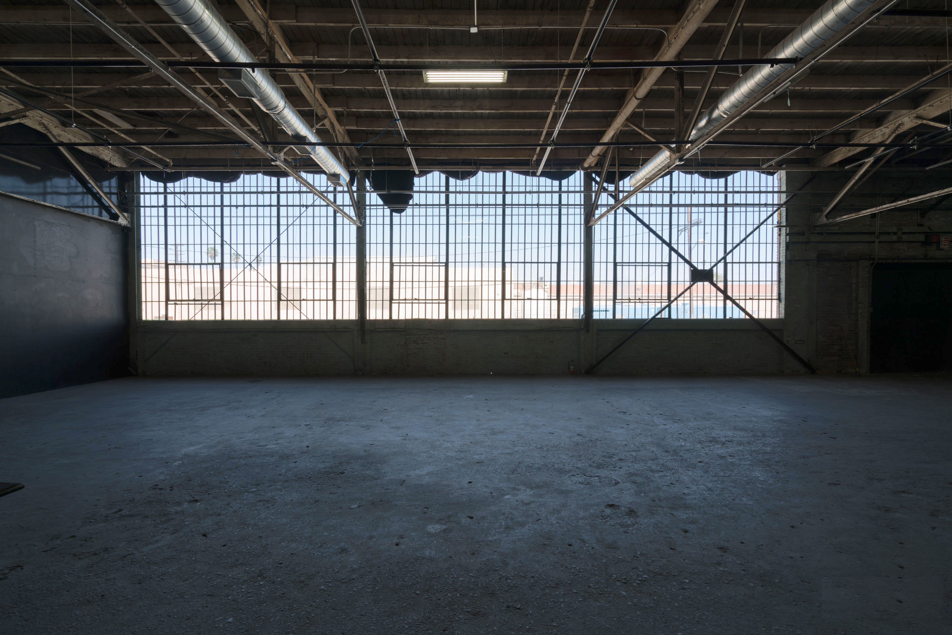 The image shows a spacious, industrial-style interior with large windows allowing natural light to enter, and a concrete floor.