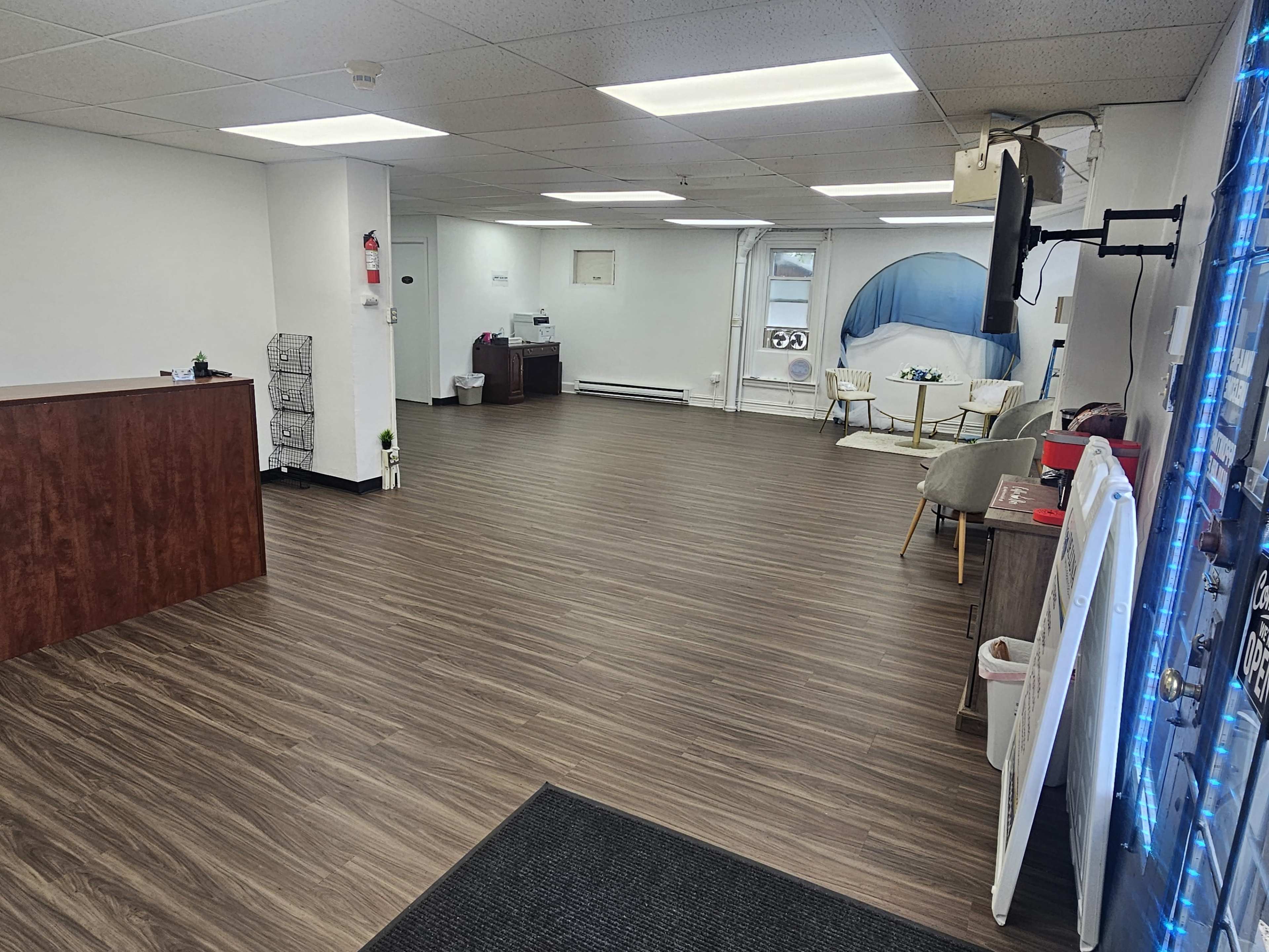 The image shows a spacious and empty commercial interior with a wooden reception desk on the left and seating areas in the background.