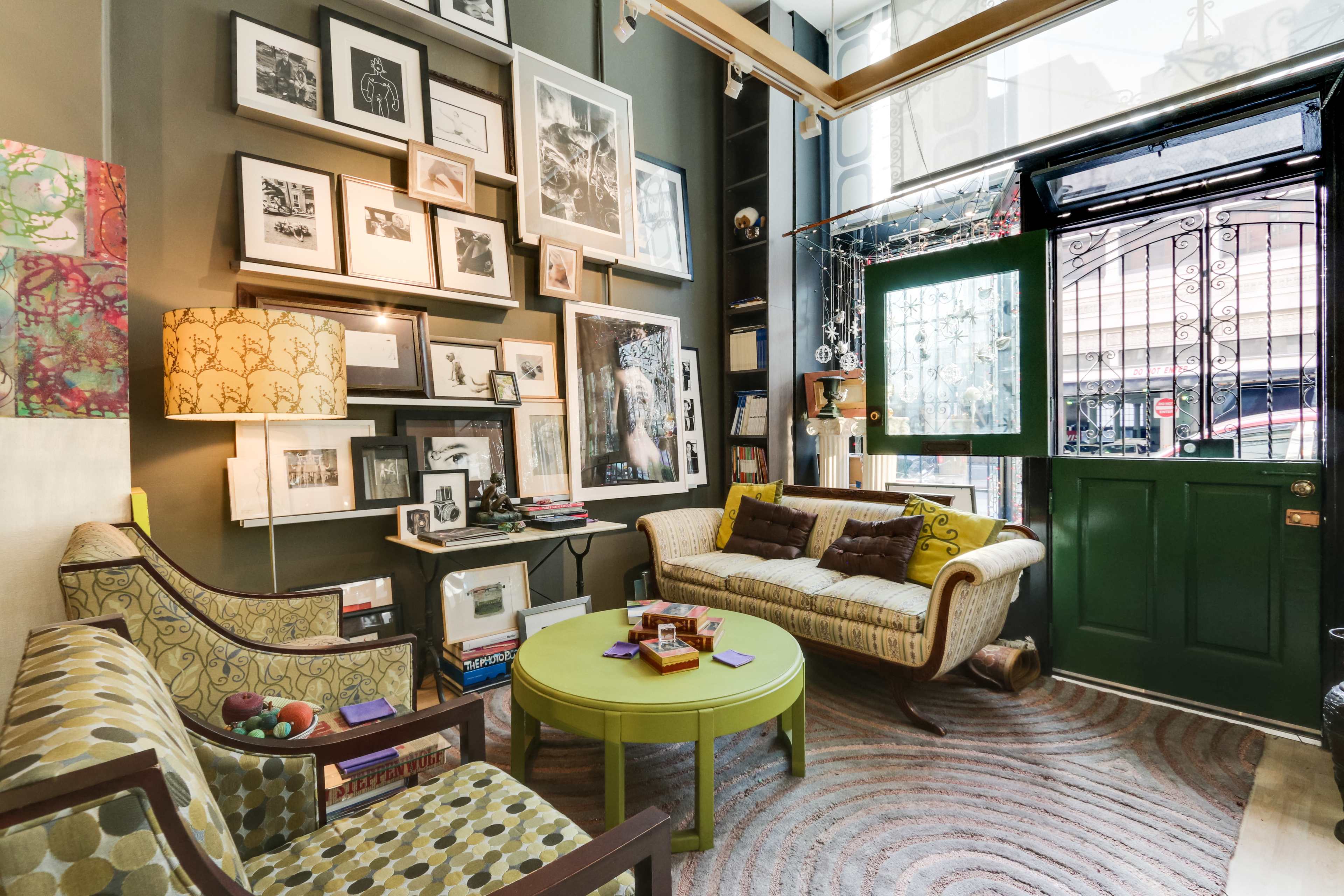 A cozy living room with a green door, a round green table, and a wall adorned with a variety of framed pictures.