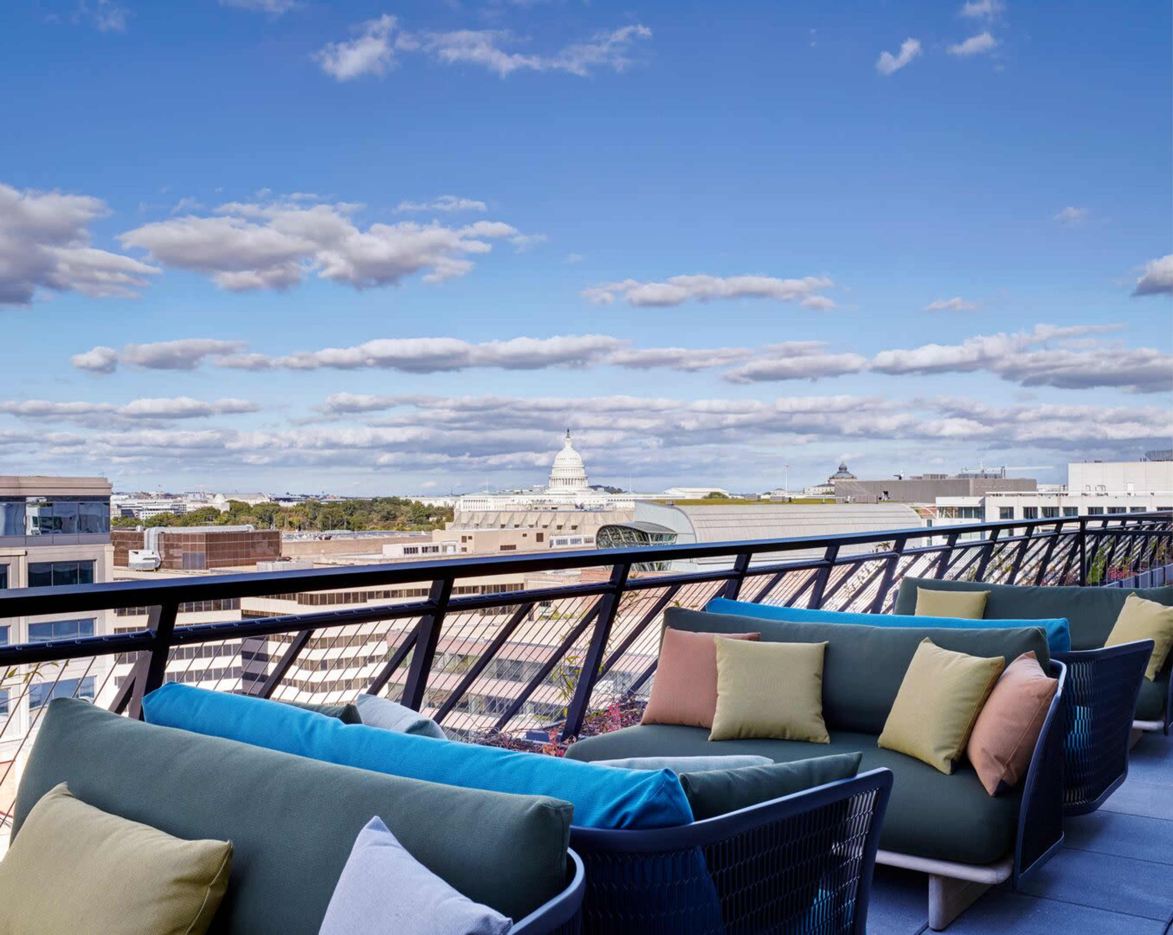 A rooftop terrace with modern seating and a view of a skyline under a partly cloudy sky.
