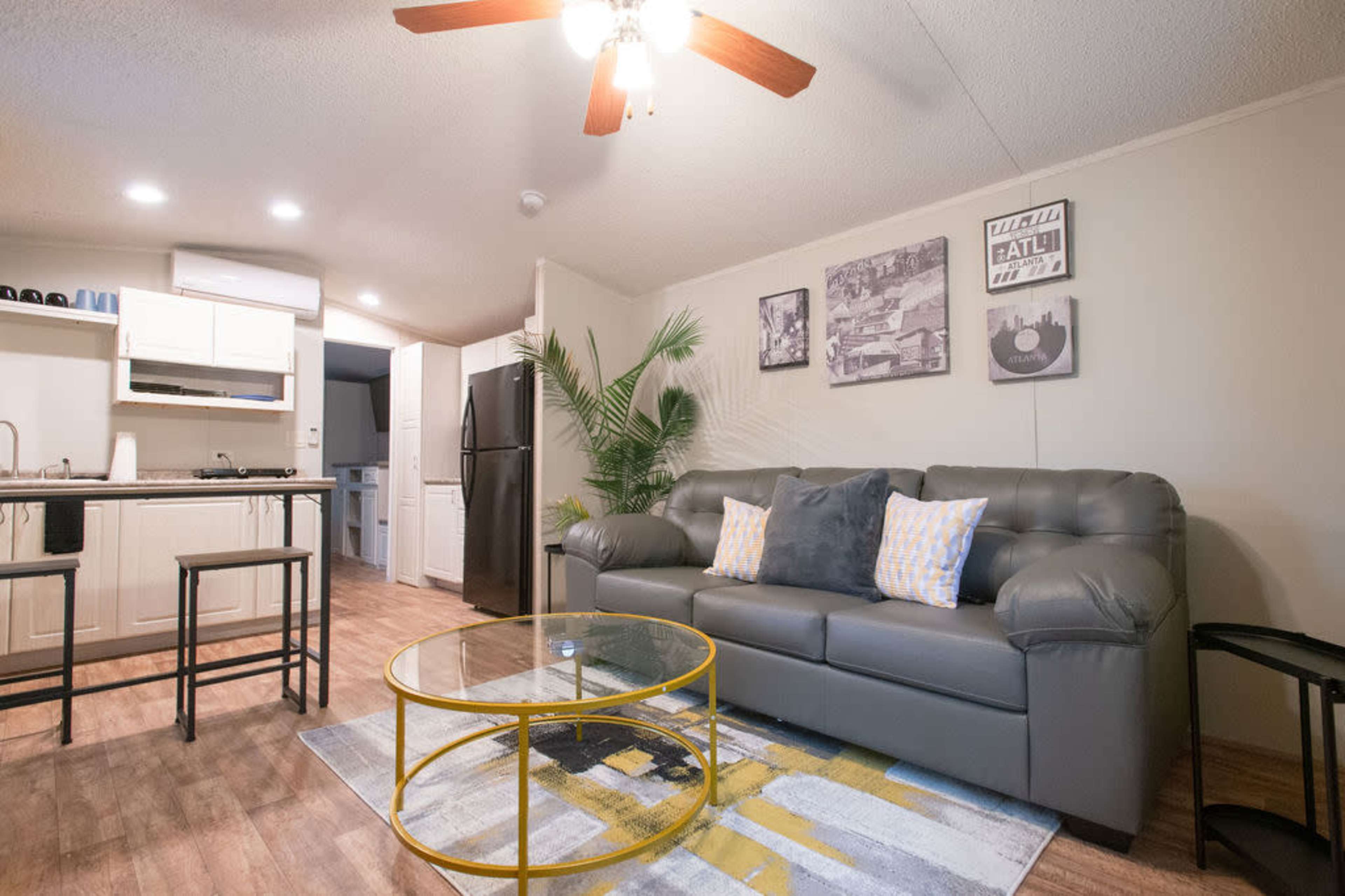 A cozy living area with a gray sofa, a round glass coffee table, and modern decor, including framed pictures on the wall and a plant in the corner.