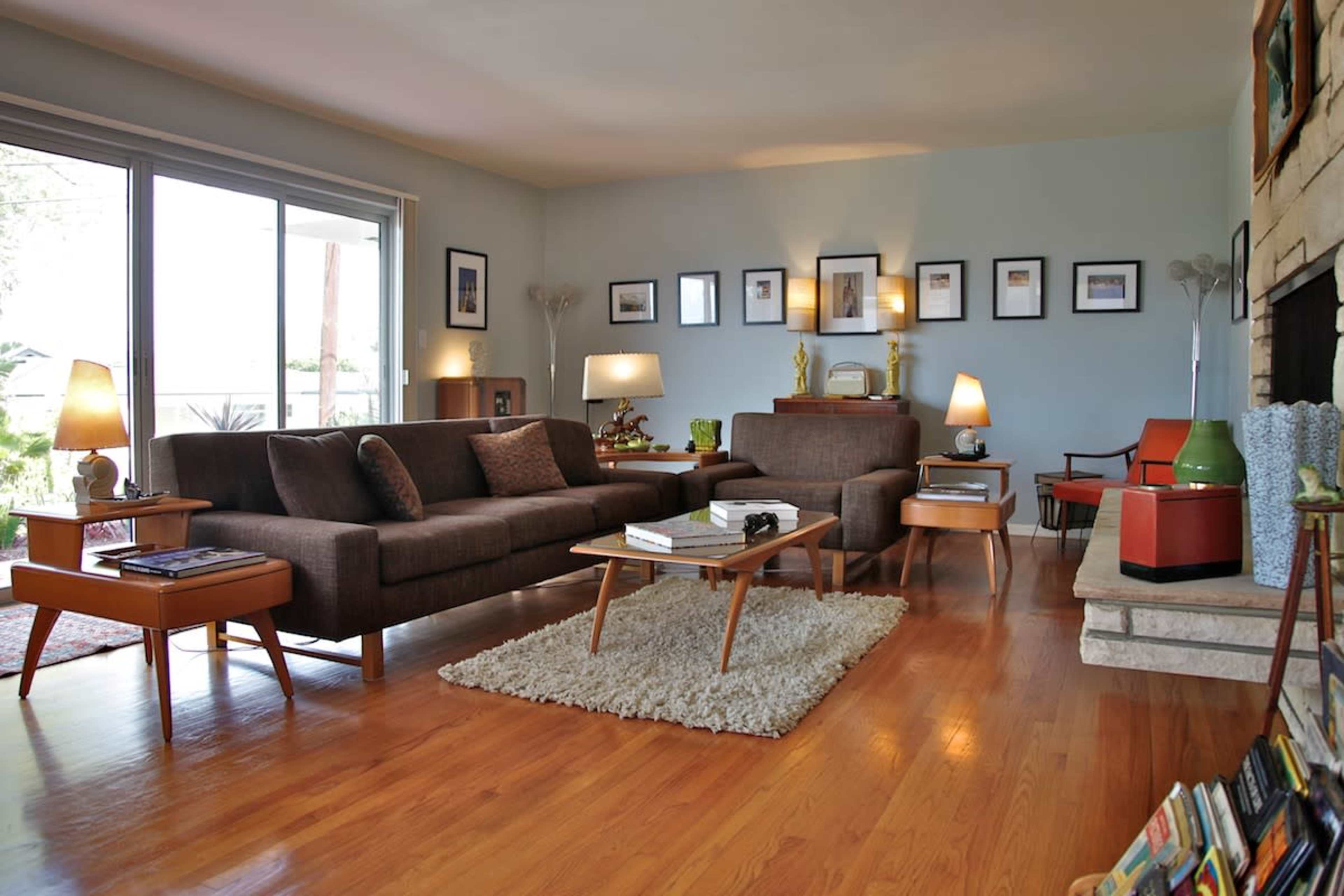 A modern living room features a brown sofa, wooden coffee table, and various framed artworks on the walls.