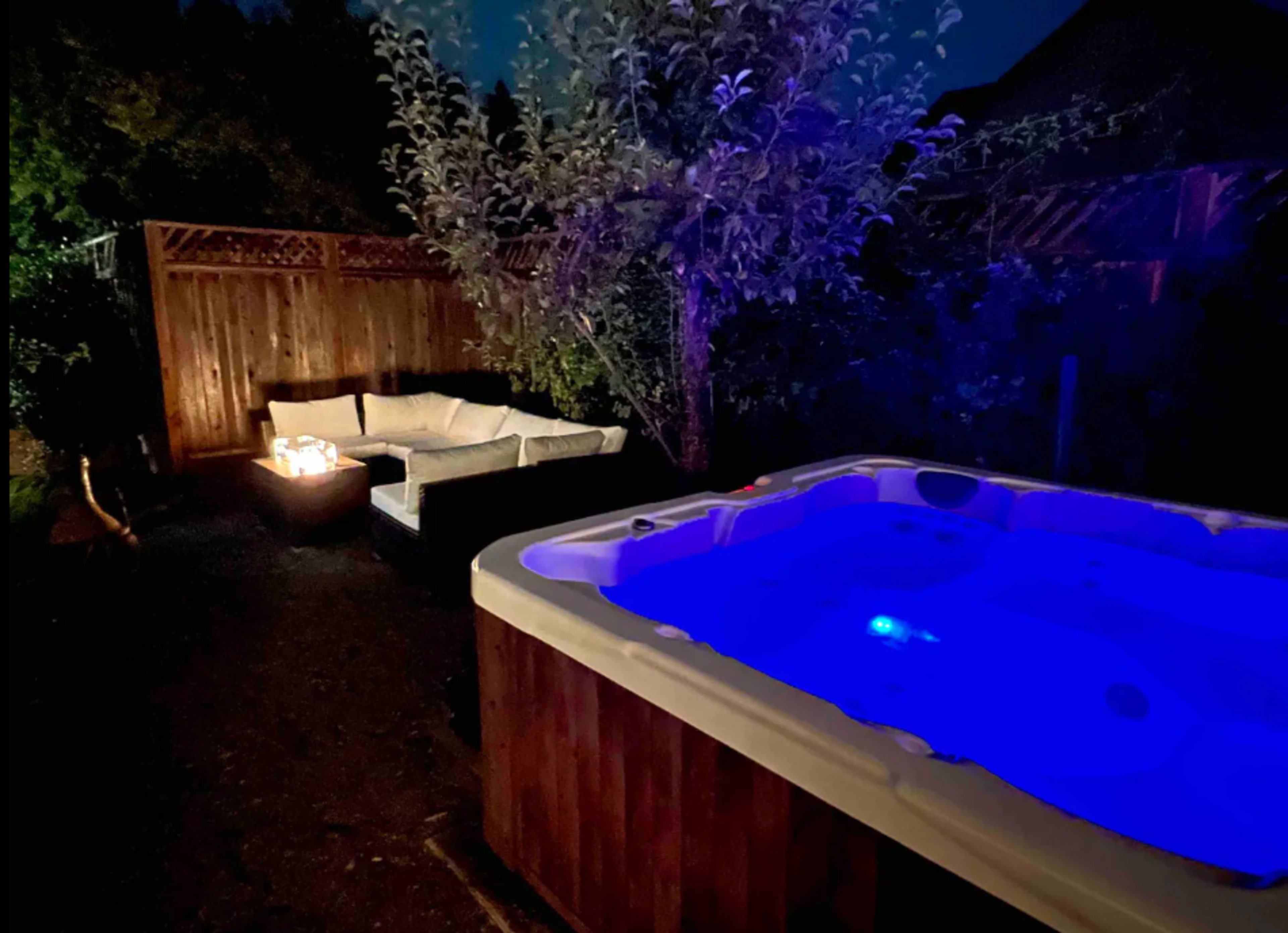 A dimly lit outdoor space featuring a hot tub with blue lighting and a seating area with a couch beside it.
