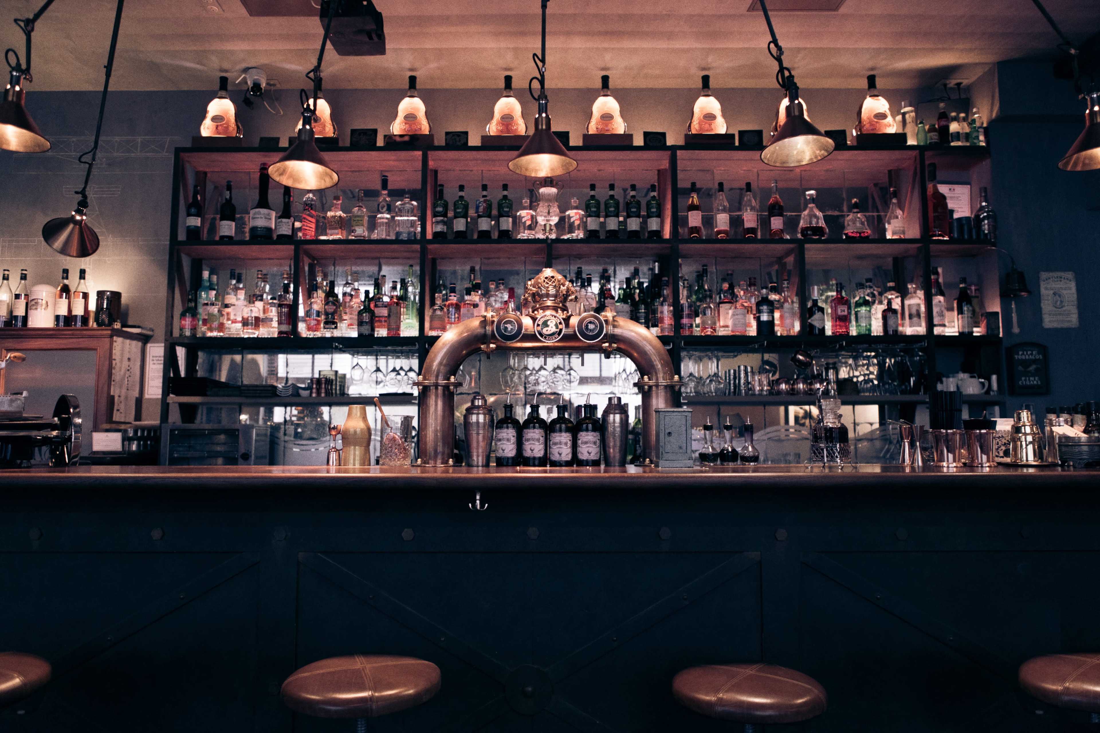 A well-lit bar with a polished counter and shelves stocked with various bottles of liquor and glassware.