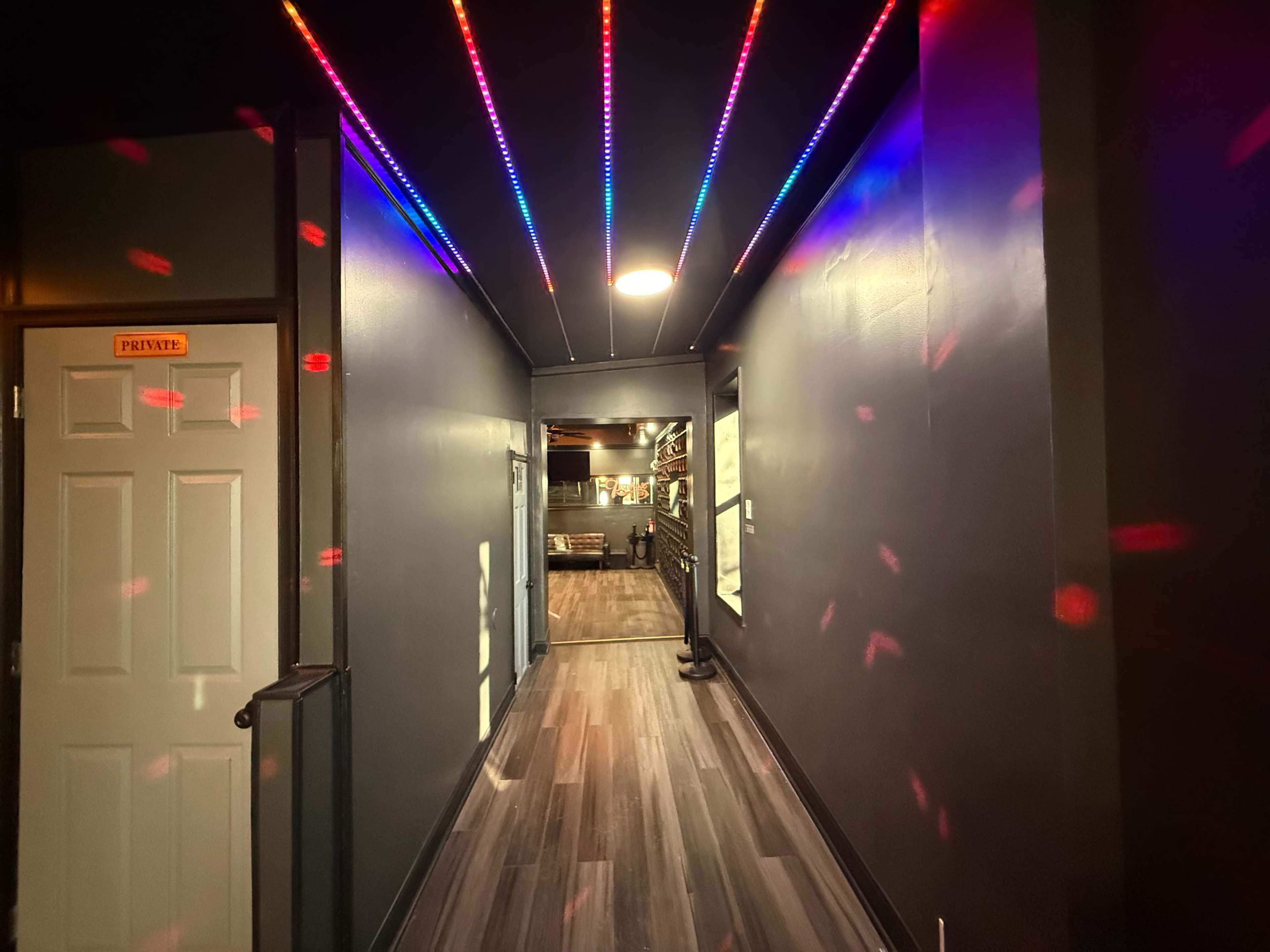 A dimly lit hallway features colorful LED lights lining the ceiling, leading to a room with shelves and a door labeled "PRIVATE."