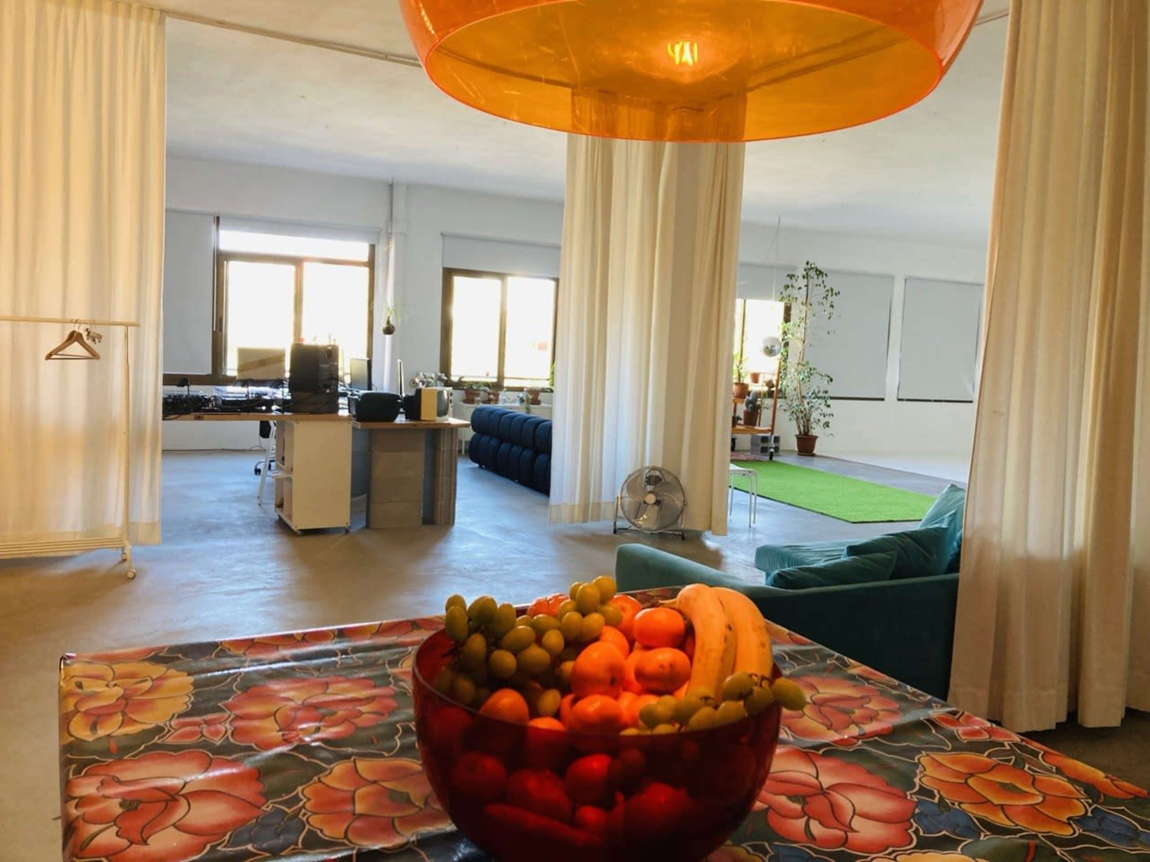 A spacious, modern interior features a dining table with a bowl of fruit, a green sofa, and large windows allowing natural light to fill the room.