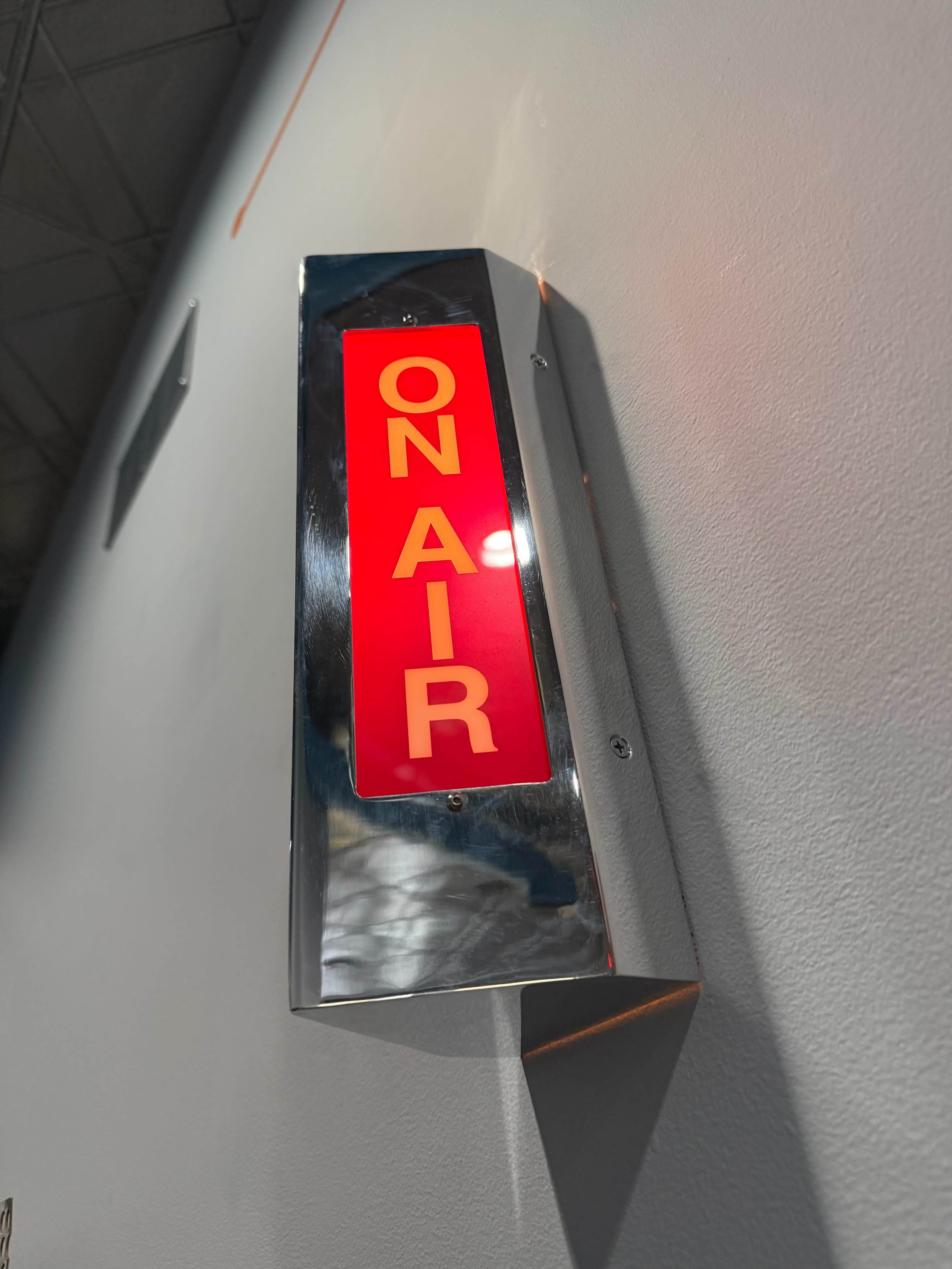 A red "ON AIR" sign is illuminated on a metallic fixture mounted on a wall.