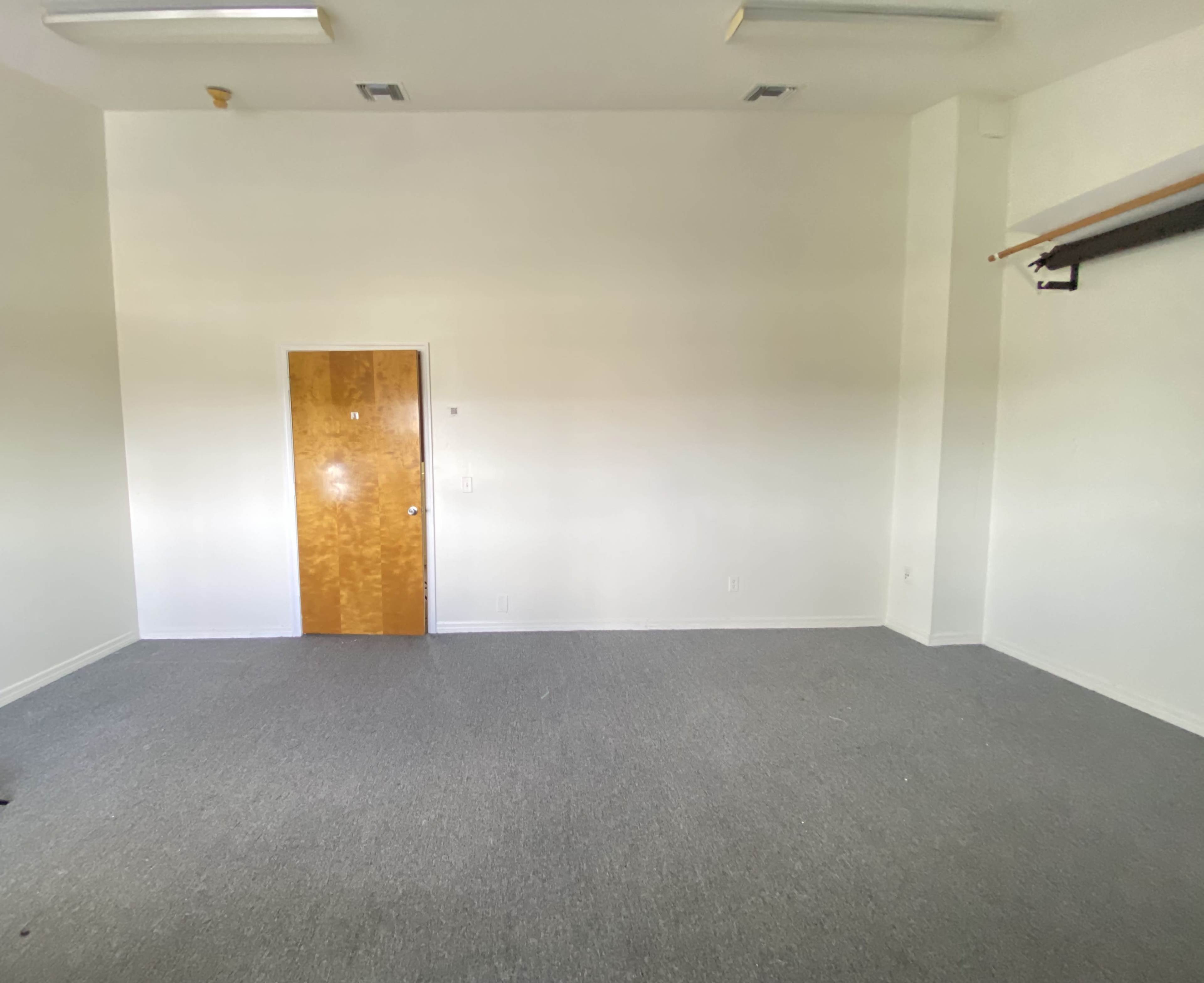 The image shows a sparsely furnished room with gray carpet and a wooden door on one wall.