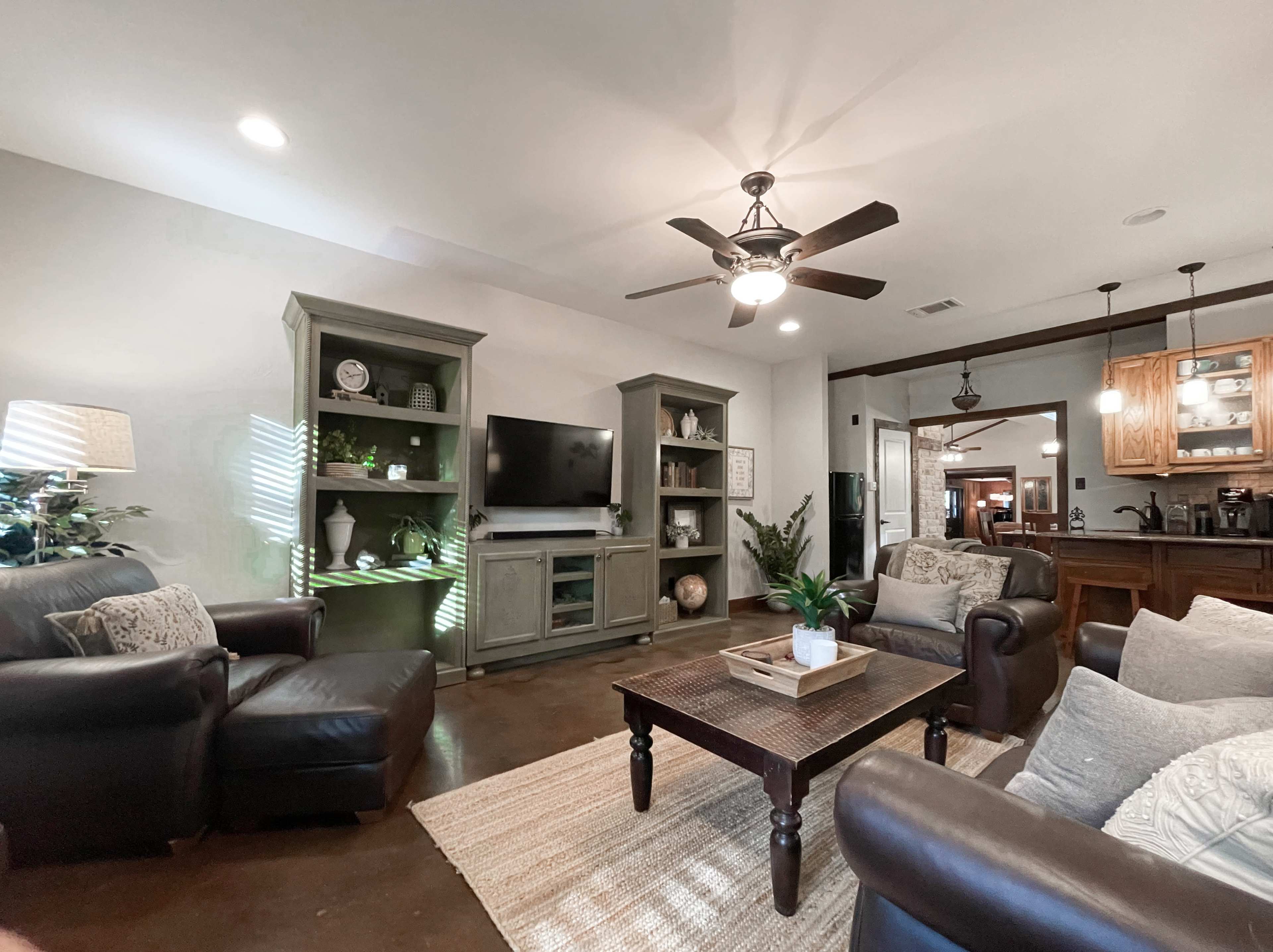 The living room features dark leather seating, a wooden coffee table, and built-in shelves surrounding a television.
