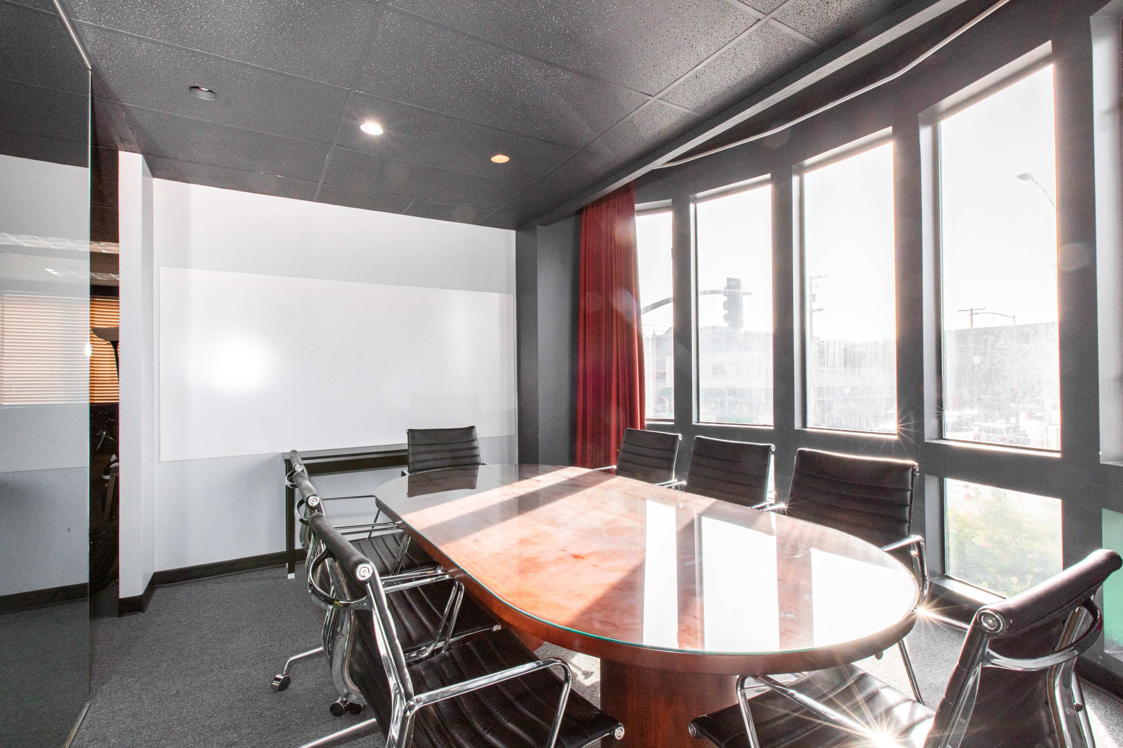 The image shows a modern conference room with a large oval table surrounded by black chairs and large windows allowing natural light.