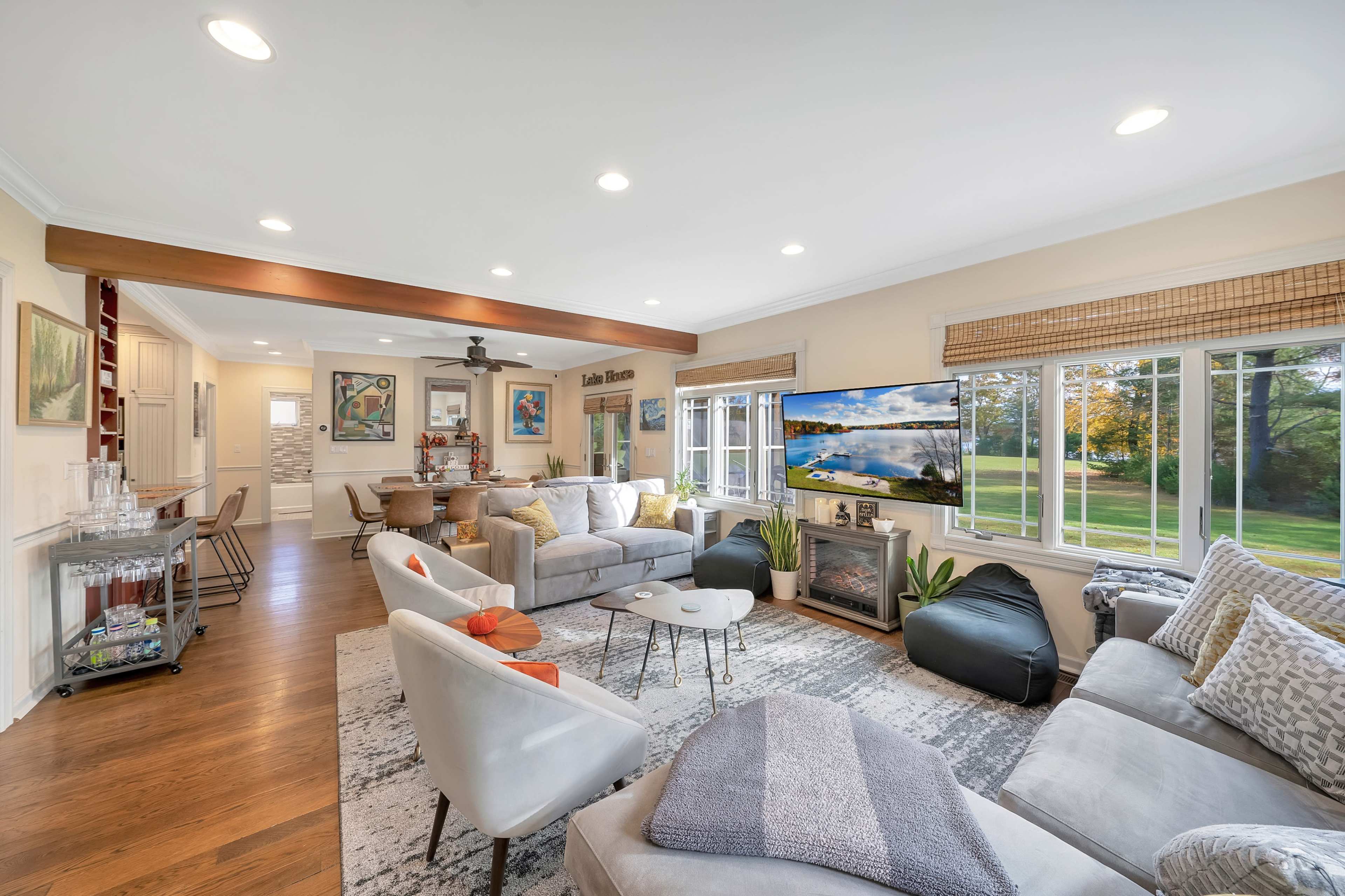 A bright, modern living room with large windows, comfortable seating, and a flat-screen television mounted on the wall.