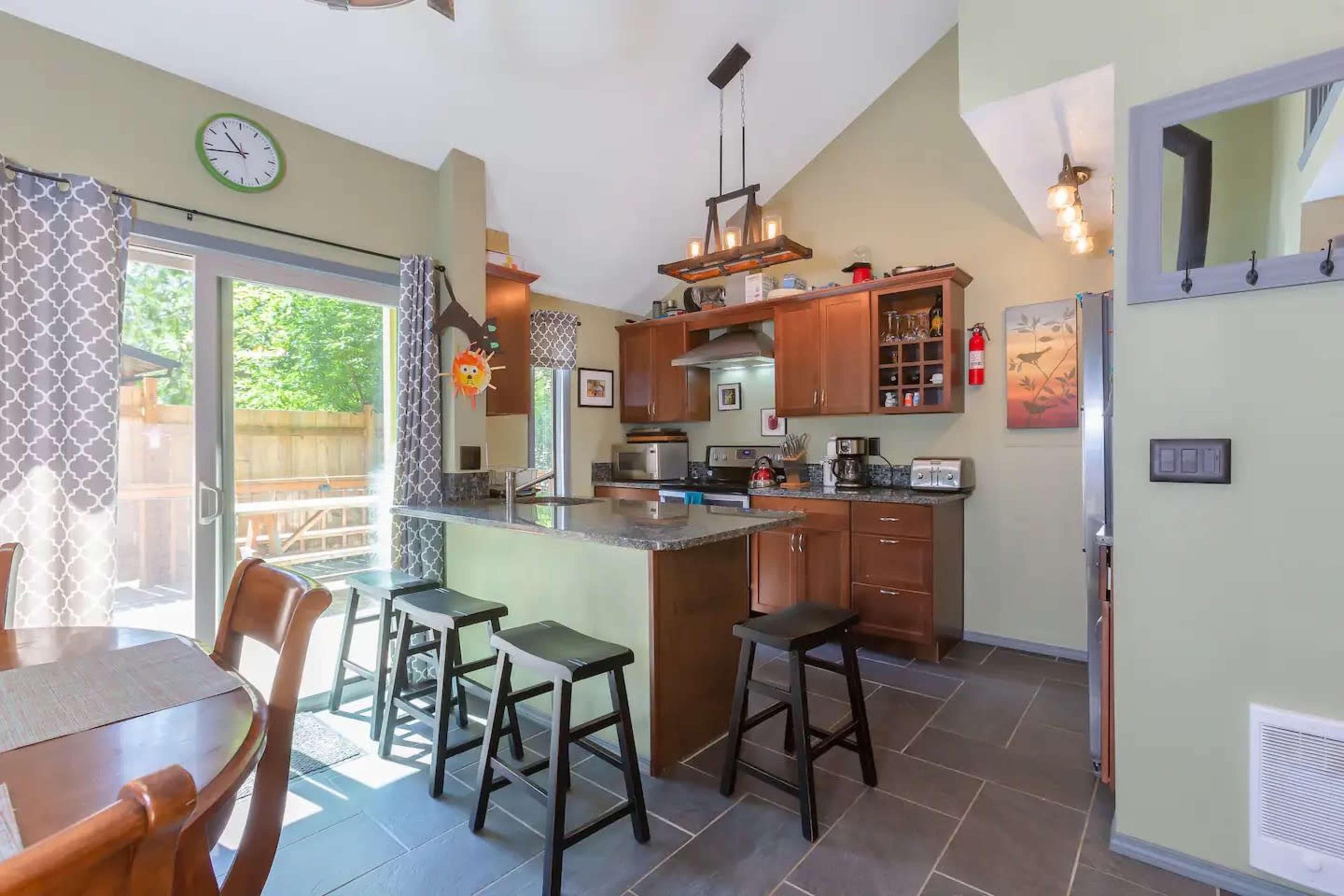 The kitchen features modern cabinetry, a central island with seating, and a dining area near large windows.