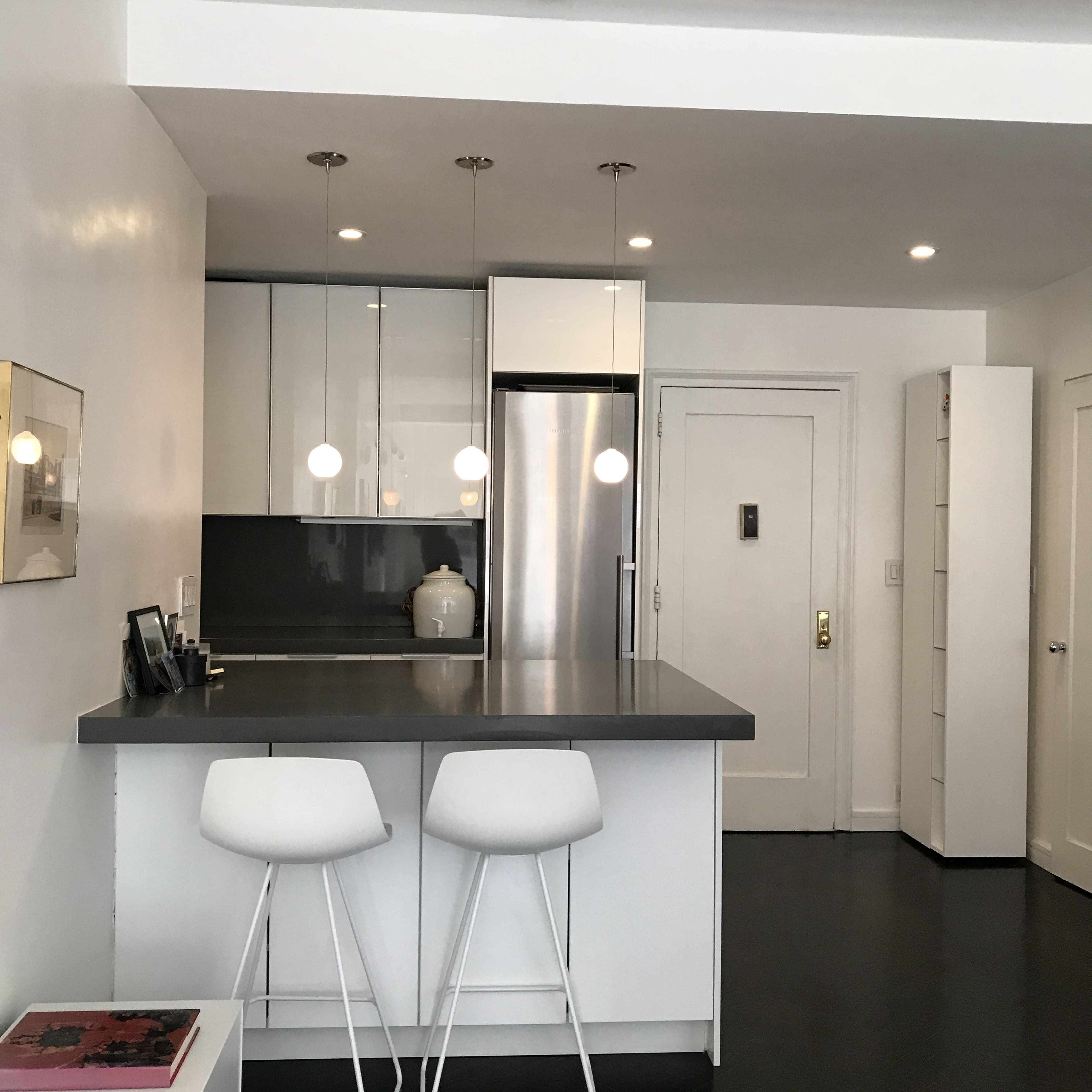 A modern kitchen with white cabinetry, a gray countertop, and two white bar stools at the counter.