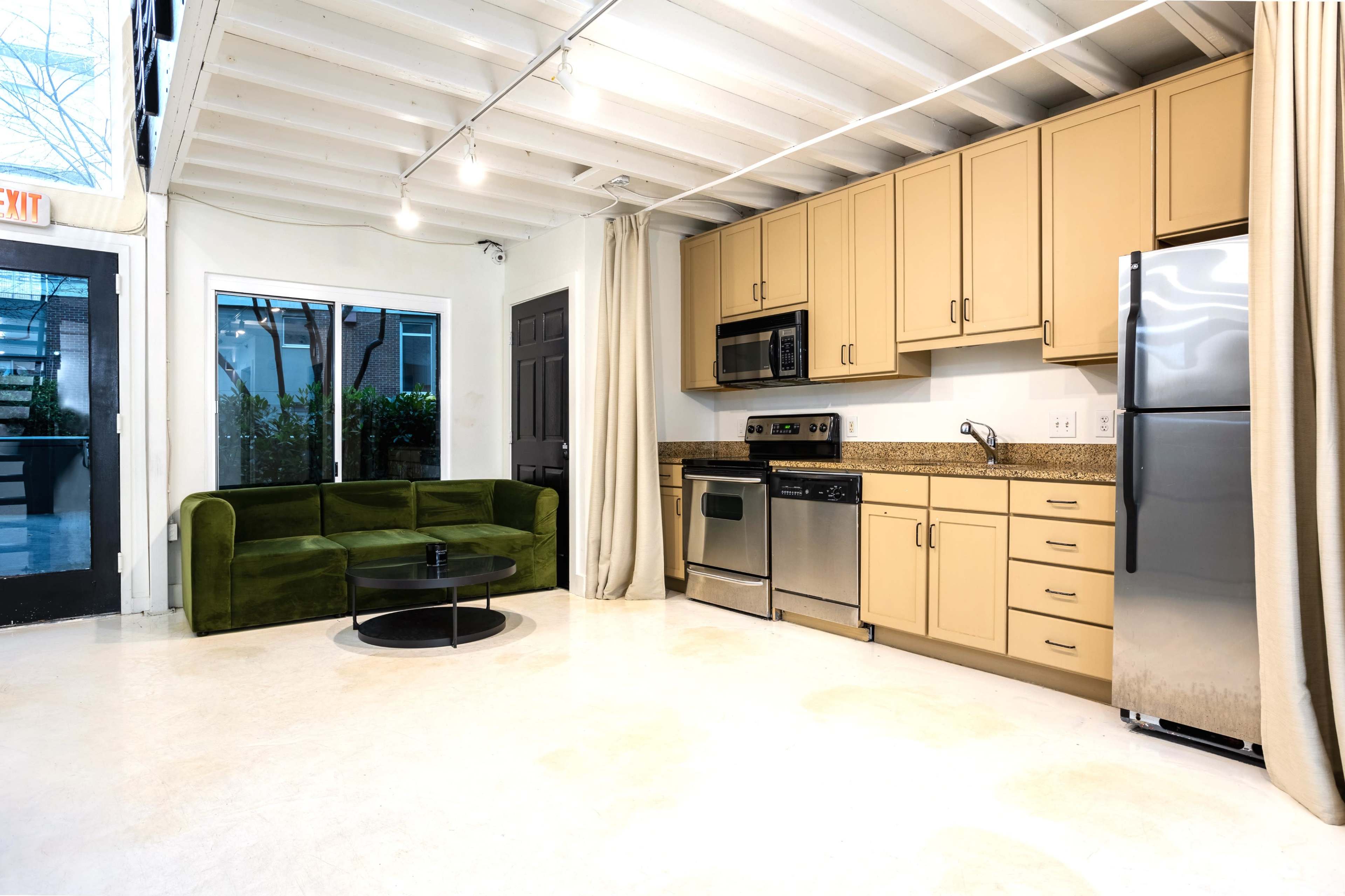 A modern kitchen and living area featuring a green couch, stainless steel appliances, and light-colored cabinetry.