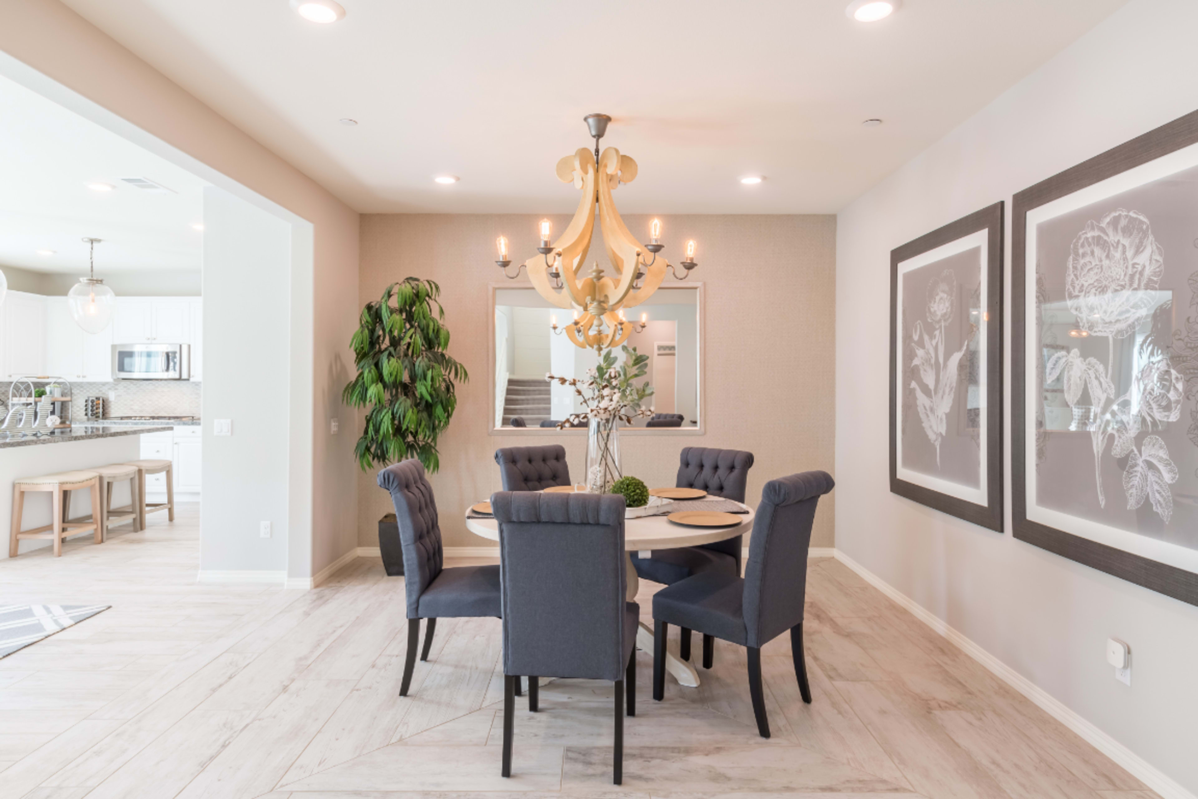A dining area features a round table surrounded by upholstered chairs, with a large chandelier overhead and framed artwork on the walls.
