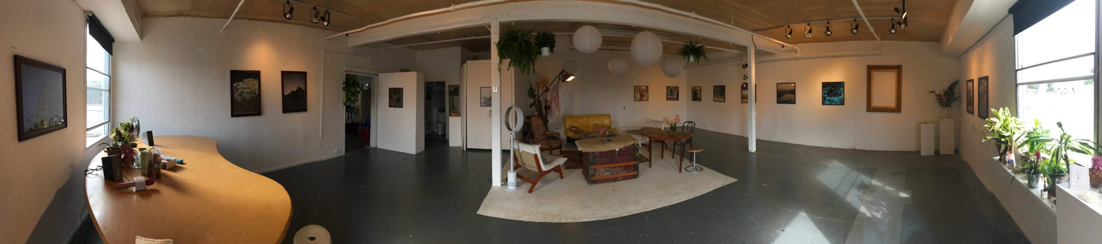 An art gallery with a circular seating area, wooden furniture, and various framed artworks displayed on the walls.