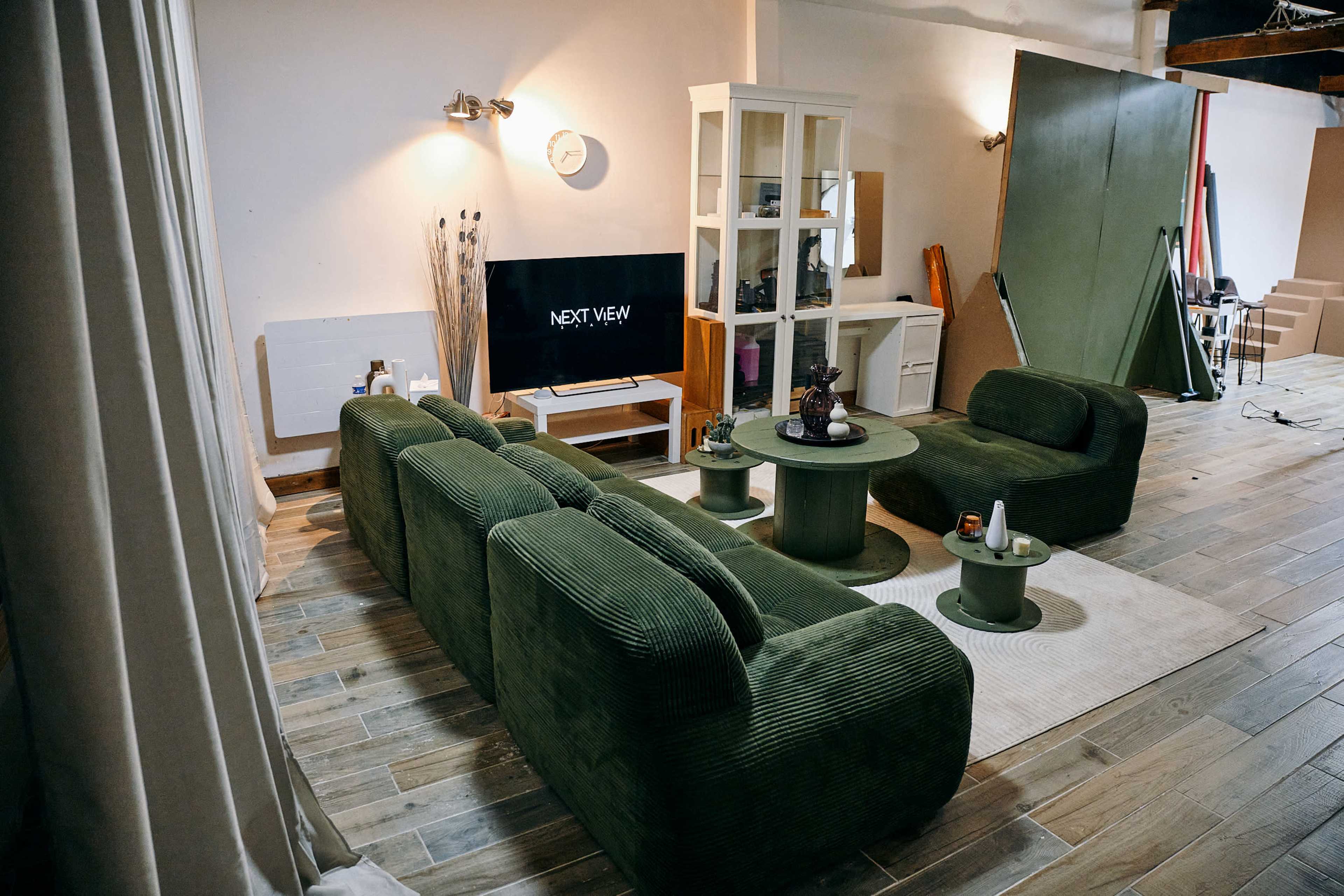 A modern living room features a green corduroy sofa set, a circular coffee table, and a television mounted on the wall.