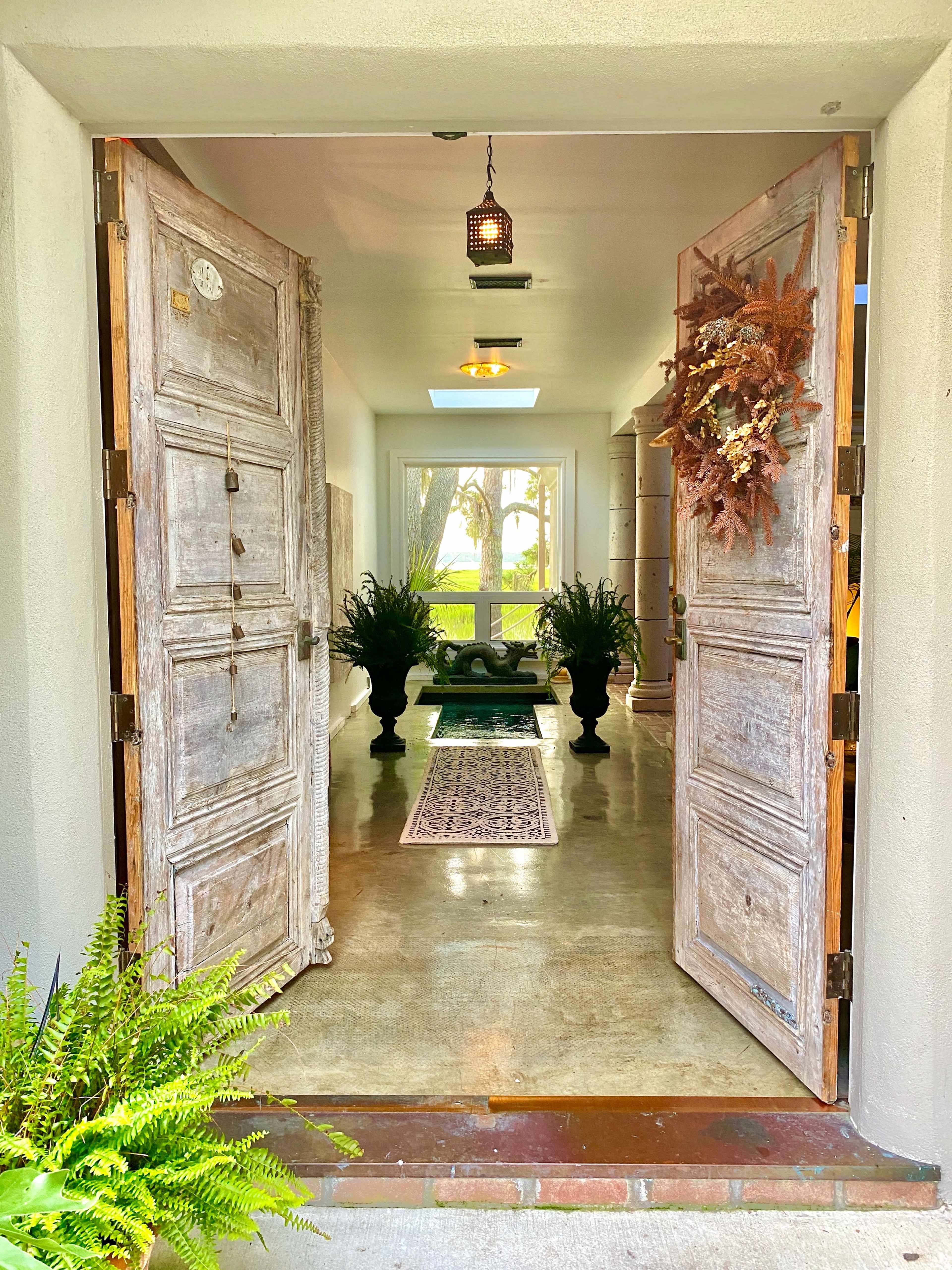An entrance with large wooden doors open to a hallway featuring a view of greenery beyond.