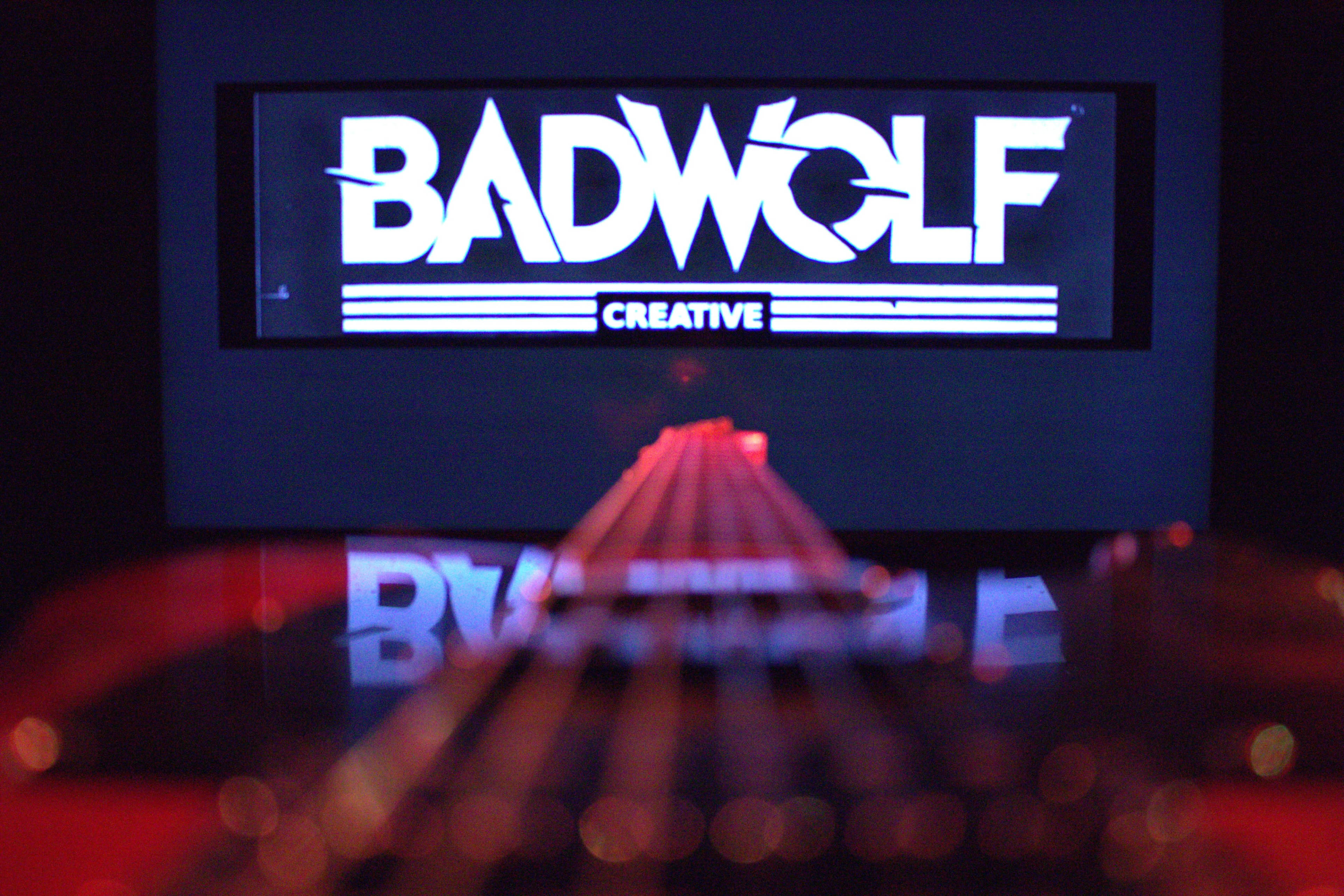 A close-up of a guitar neck extends toward a large screen displaying the logo "BADWOLF CREATIVE."