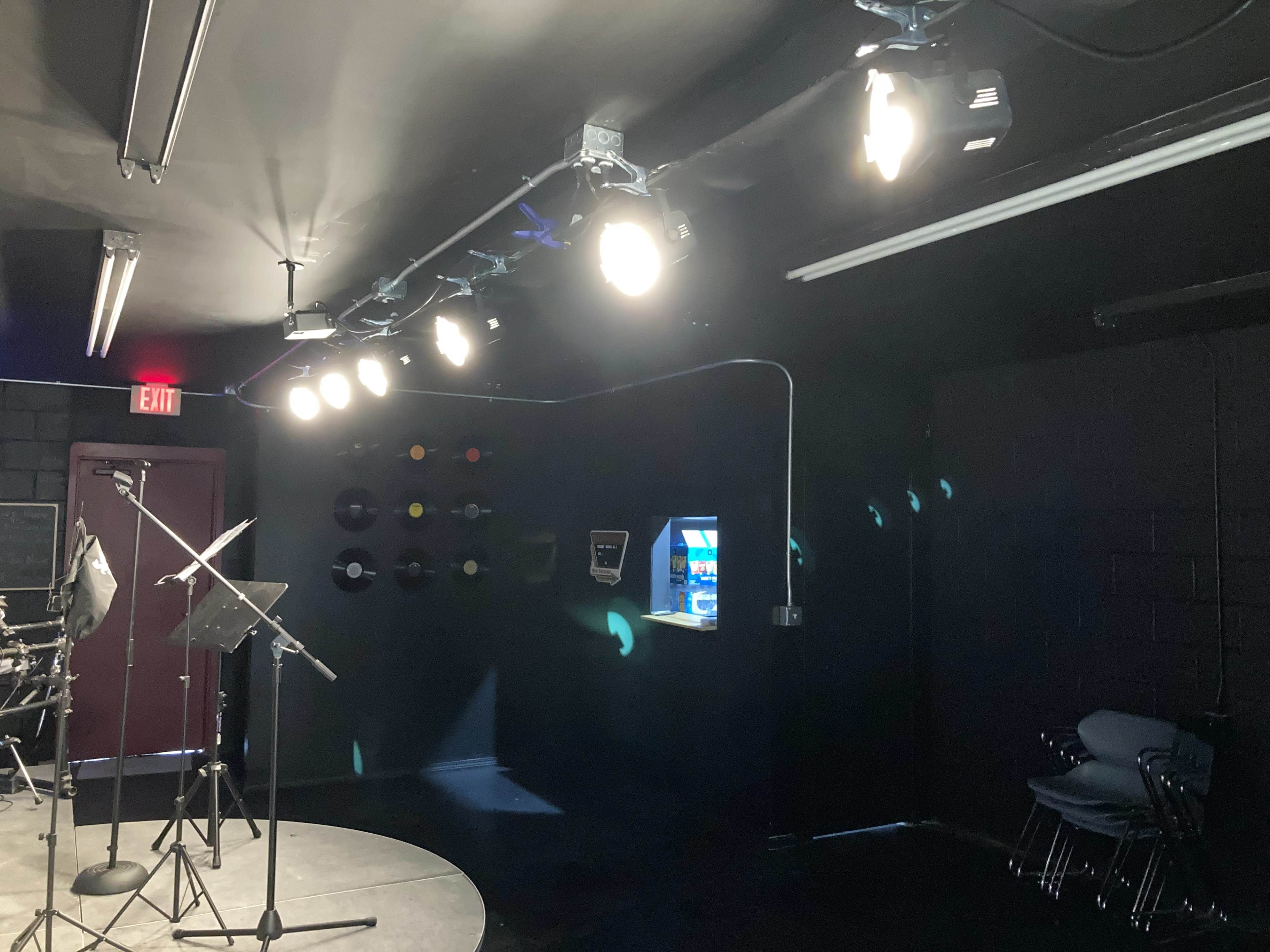 A dimly lit music studio with a circular stage, illuminated by overhead lights, and a wall featuring vinyl records.