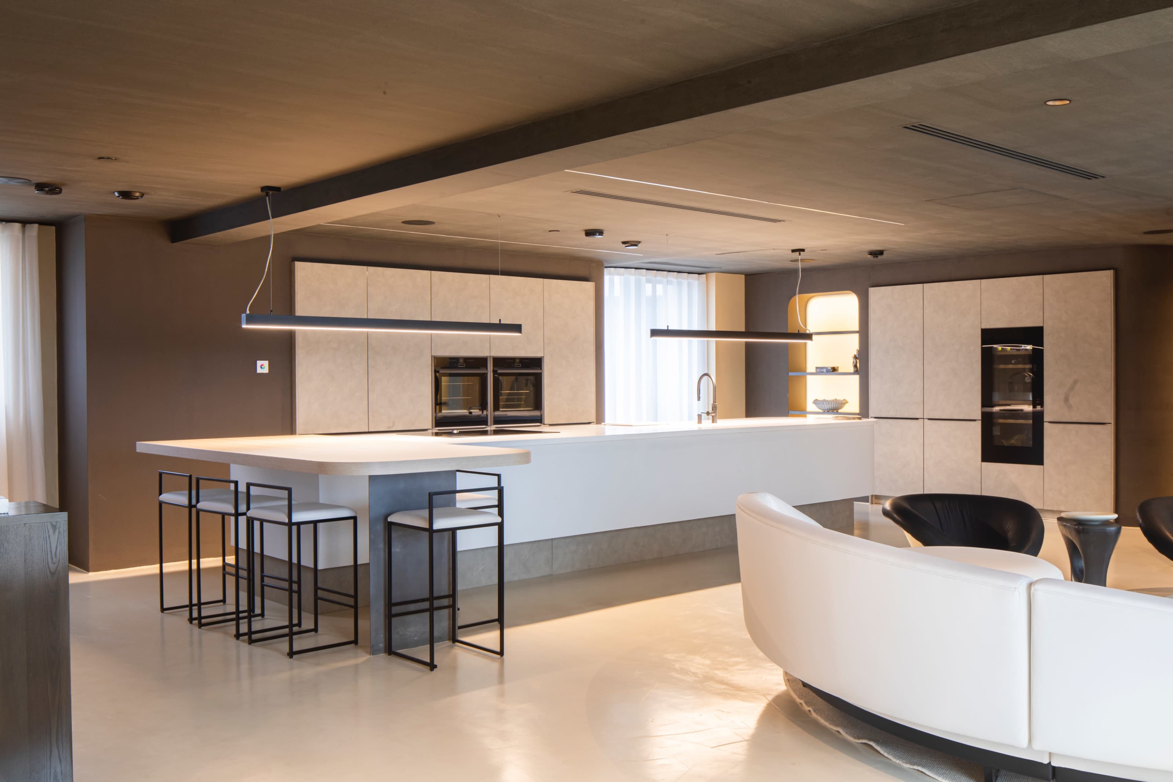 A modern kitchen features a central island with bar stools, built-in appliances, and a minimalist design.